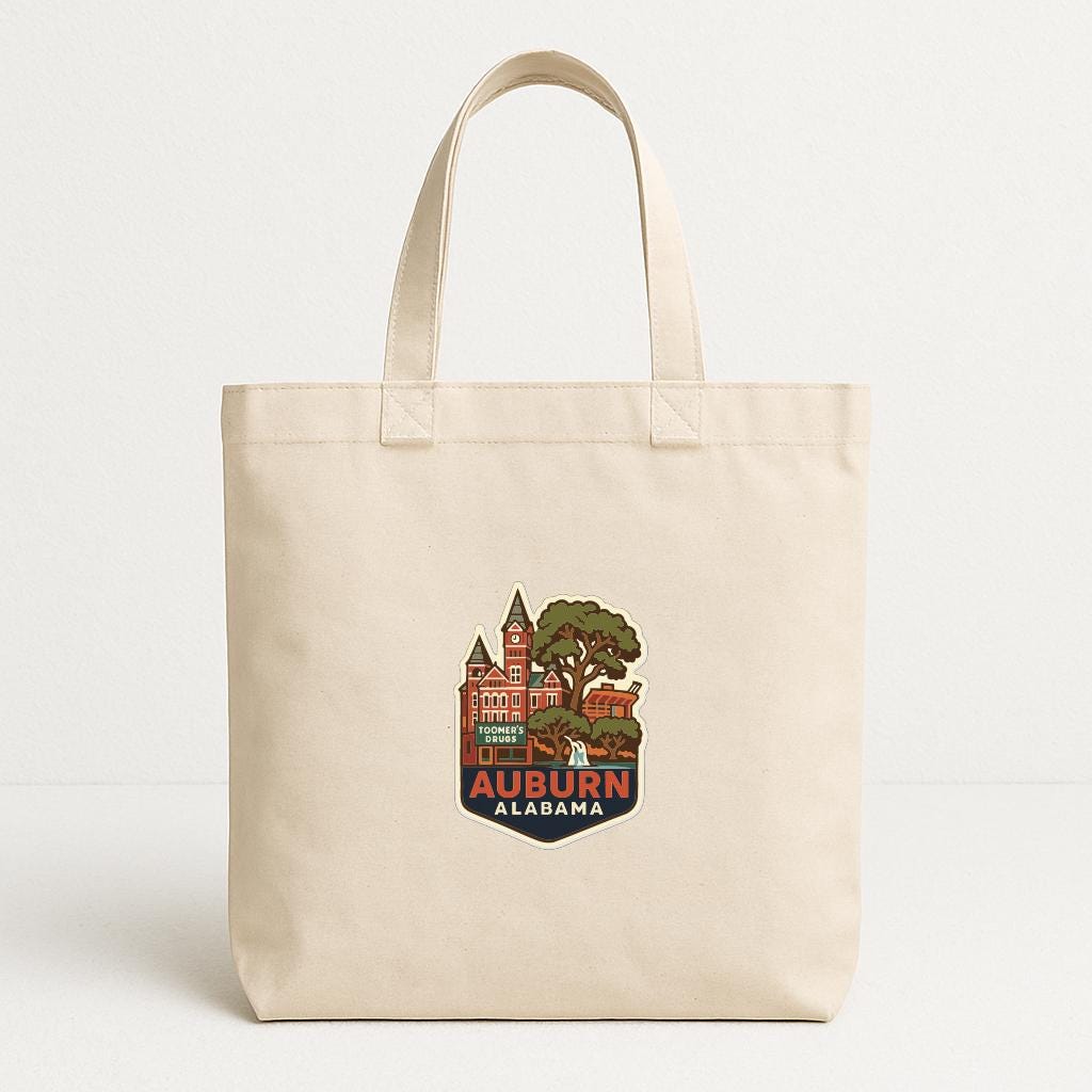 A beige tote bag with a printed design depicting a cityscape and the text "AUBURN ALASKA" printed on it.