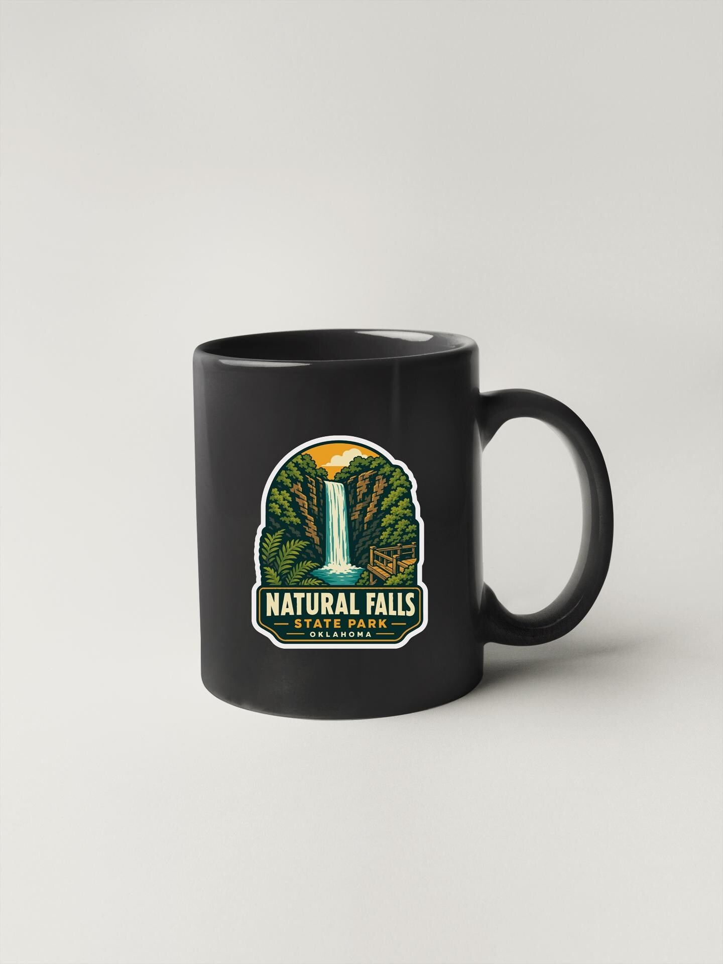 A black coffee mug with a graphic design depicting a waterfall and forest.