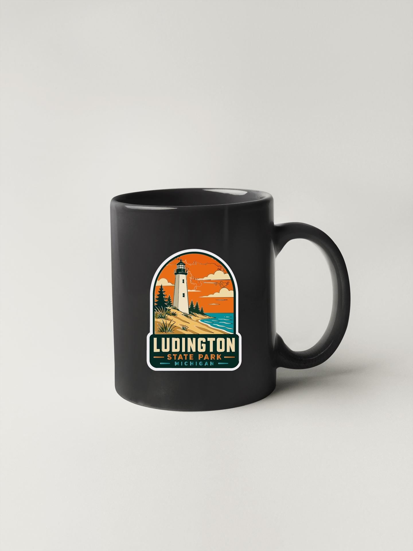 A black coffee mug with a graphic design featuring a lighthouse and a sunset landscape.