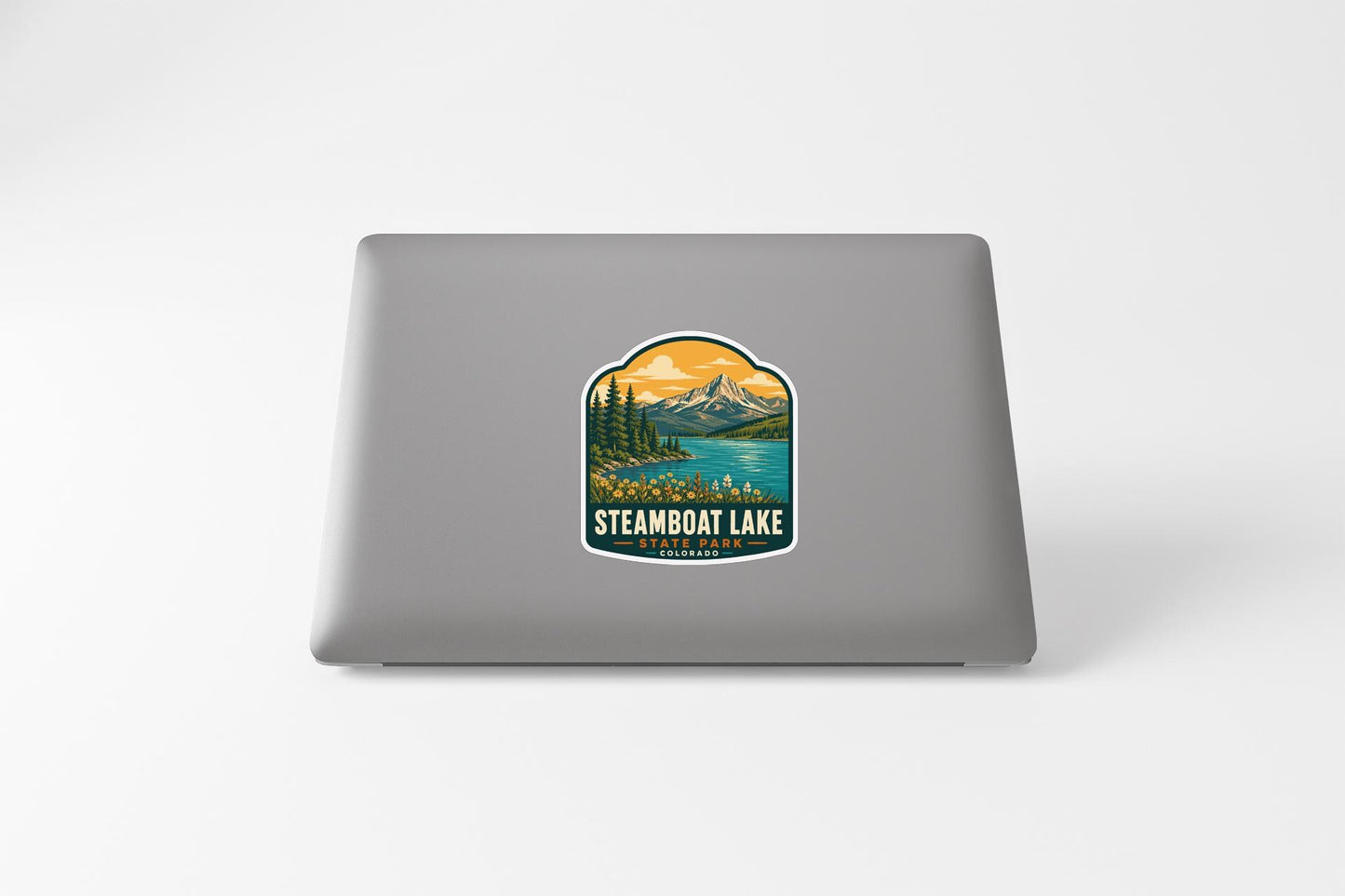 a sticker on the back of a laptop that displays a scenic mountain landscape with a lake and pine trees.