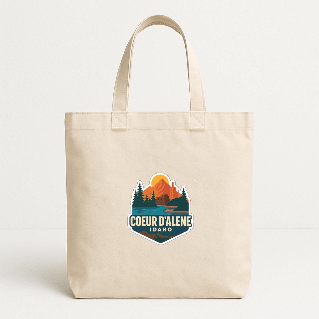 A beige tote bag with a printed logo that says "COEUR D'ALENE IDAHO".