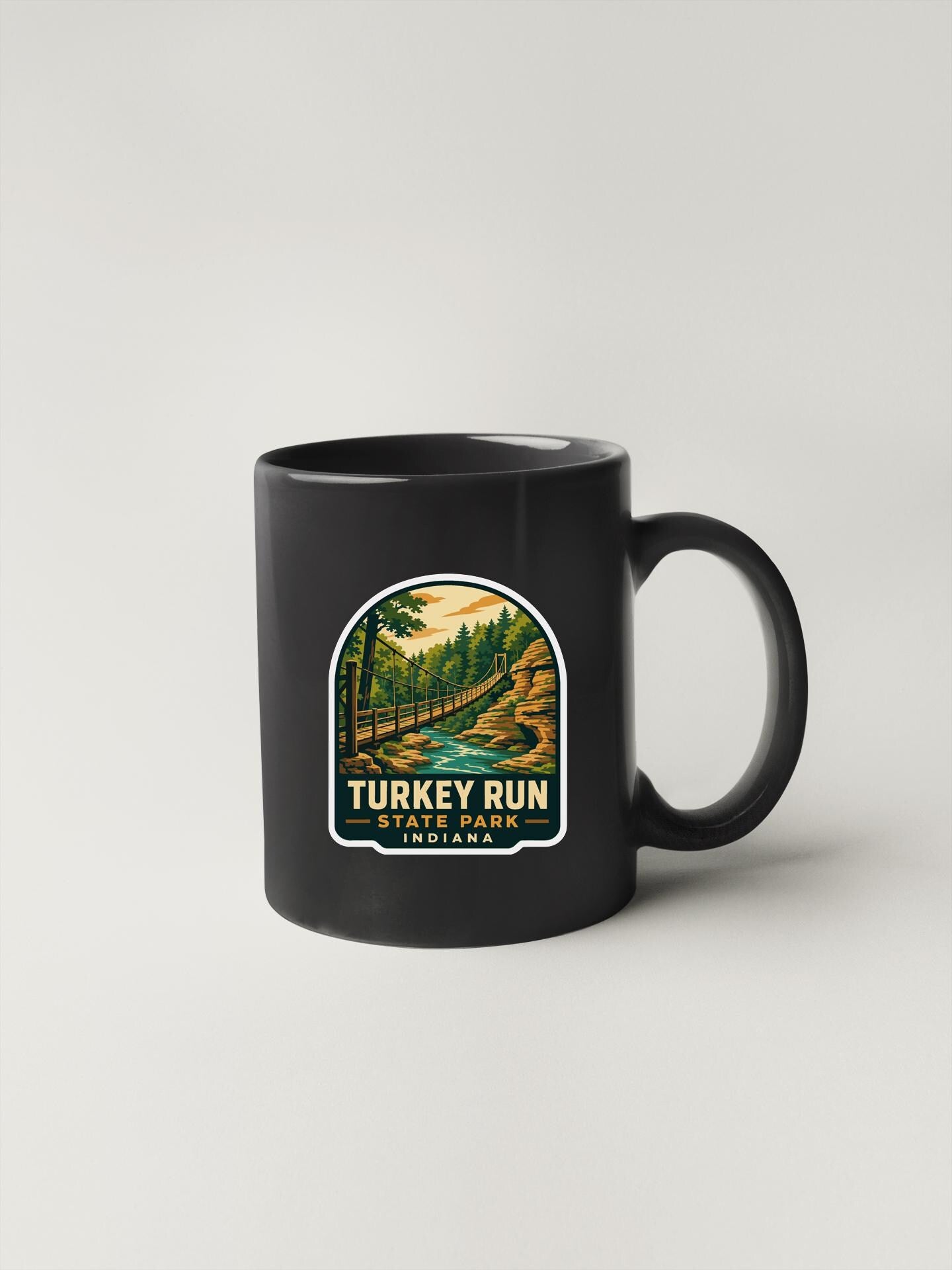 A black coffee mug with a label that says "TURKEY RUN STATE PARK INDIA" and features an illustration of a forest and a river.