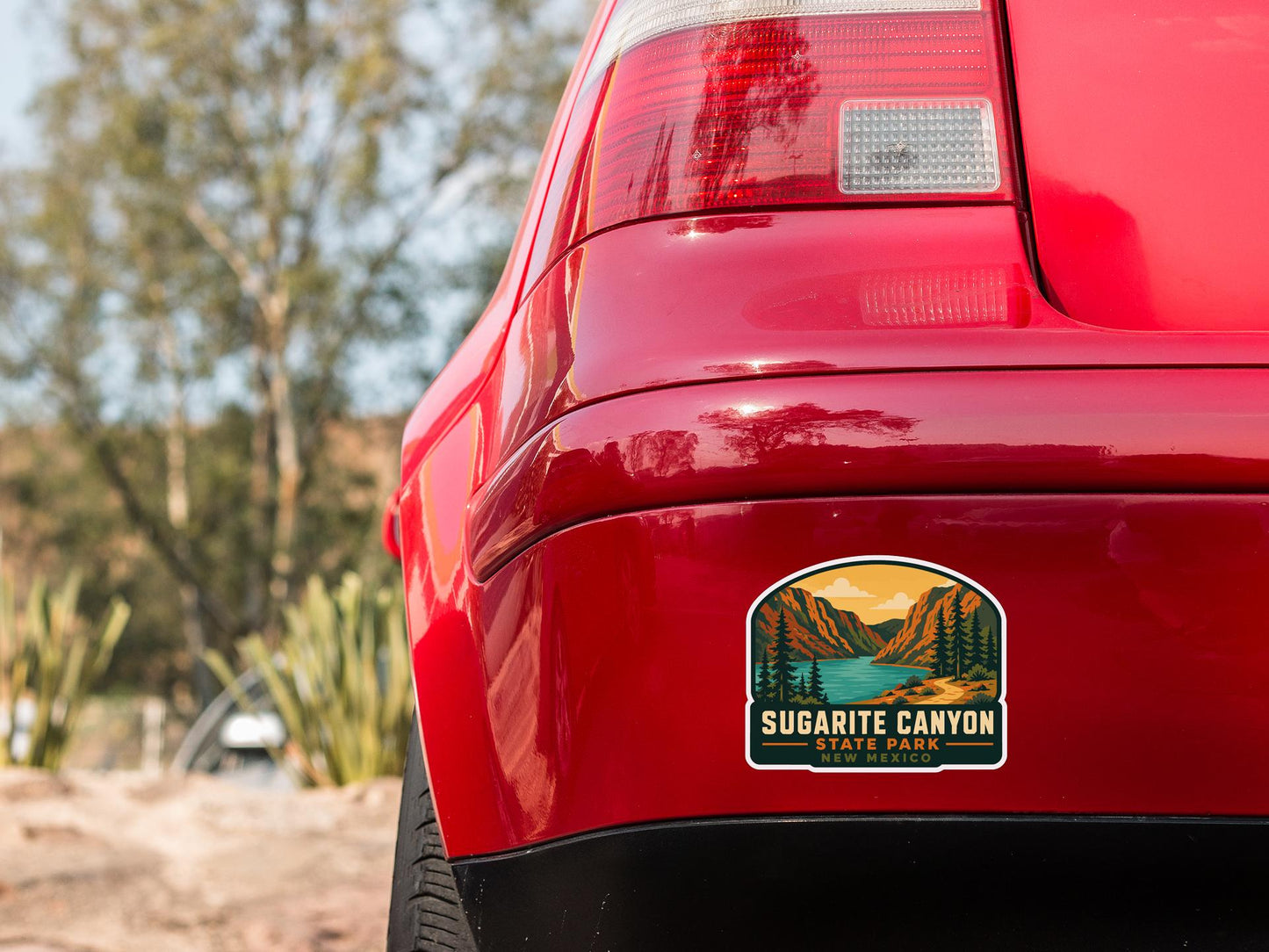 the rear end of a red car with a sticker on the trunk that says "Sugarite Canyon State Park".