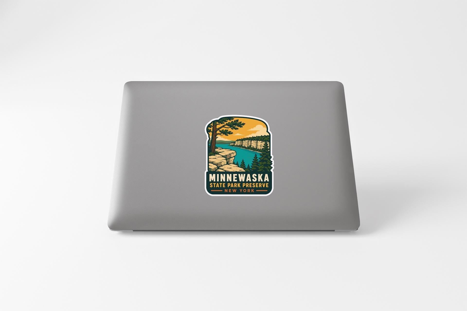 A sticker on the back of a laptop, depicting a scenic landscape with a lake, mountains, and trees.