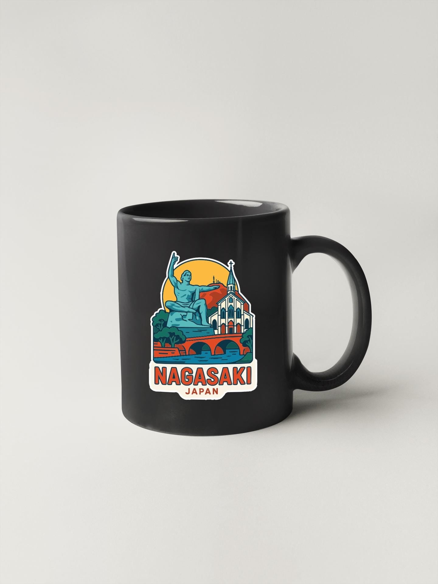 A black coffee mug with a colorful illustration of a statue and buildings, along with the text "Nagasaki Japan" printed on it.