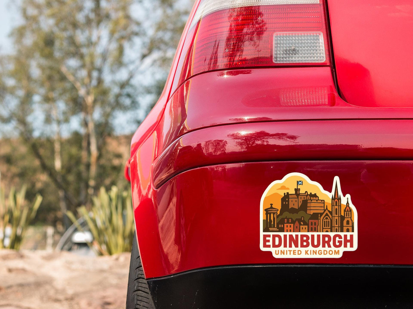the rear end of a red car with a sticker on the trunk that features the city of Edinburgh, United Kingdom.