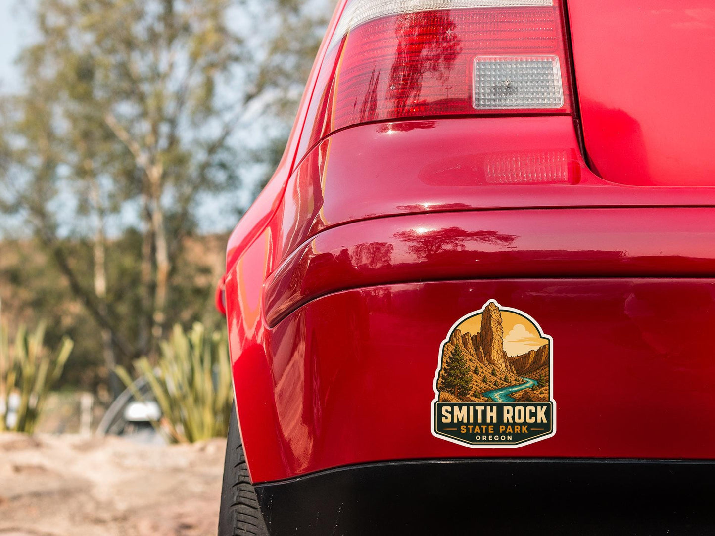 the rear end of a red car with a sticker on the bumper that says "Smith Rock State Park Oregon".