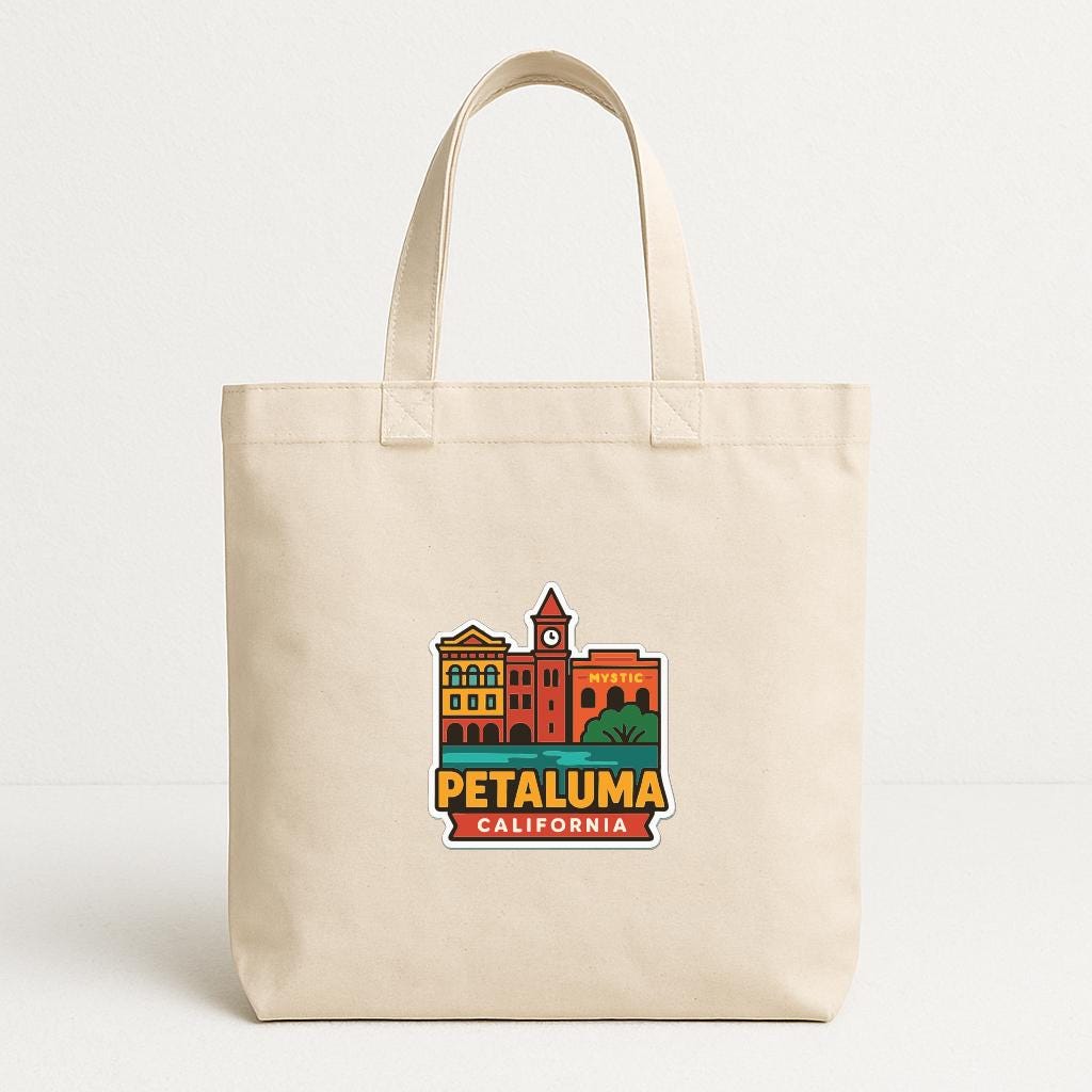 A beige tote bag with a colorful graphic of a cityscape and the text "PETALUMA CALIFORNIA" printed on it.