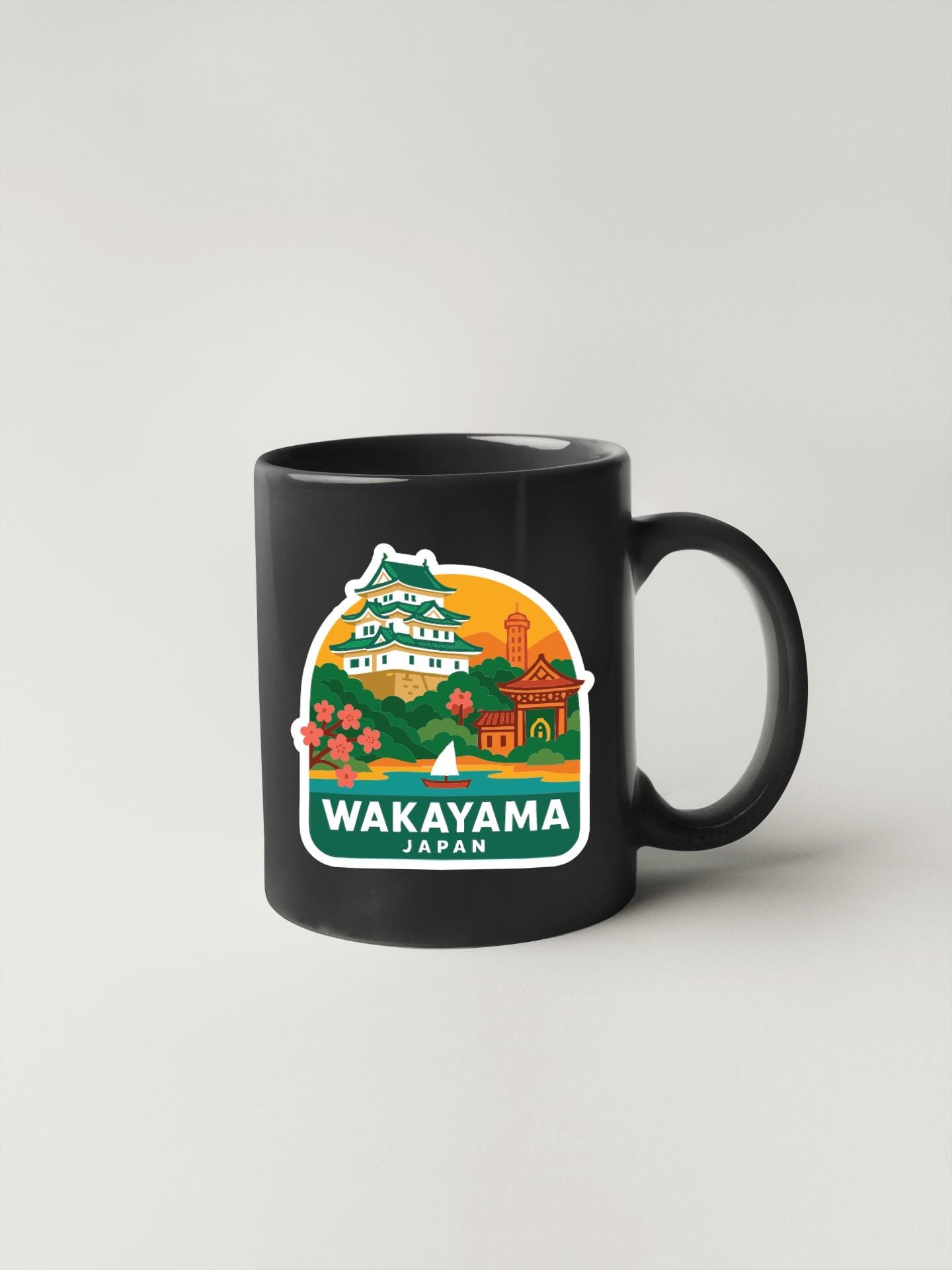 A black coffee mug with a colorful illustration of a Japanese landmark, specifically the Wakayama Castle, and the text "Wakayama Japan" printed on it.