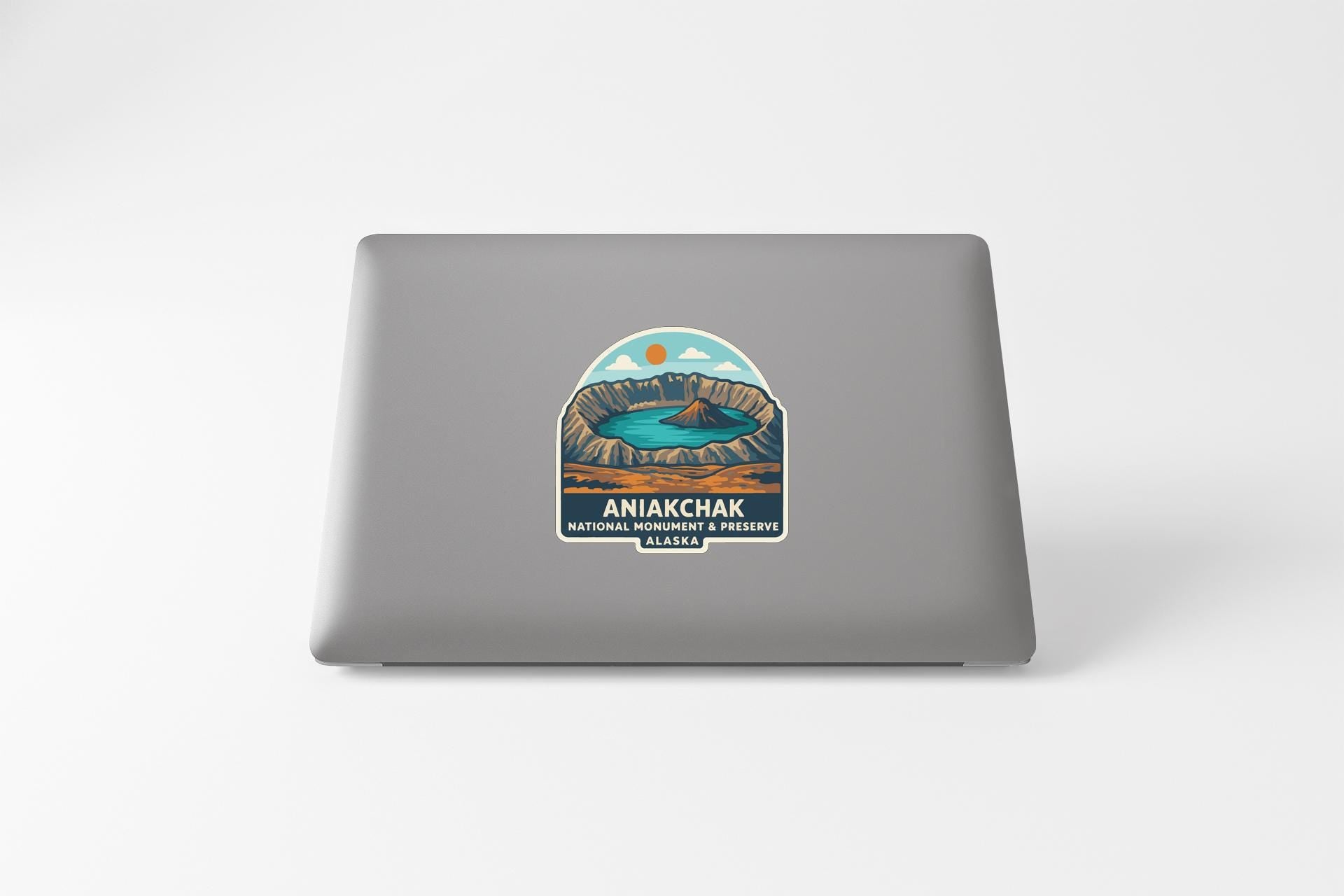 a sticker or decal on the back of a laptop, depicting a scenic landscape with mountains, a lake, and a sunset.