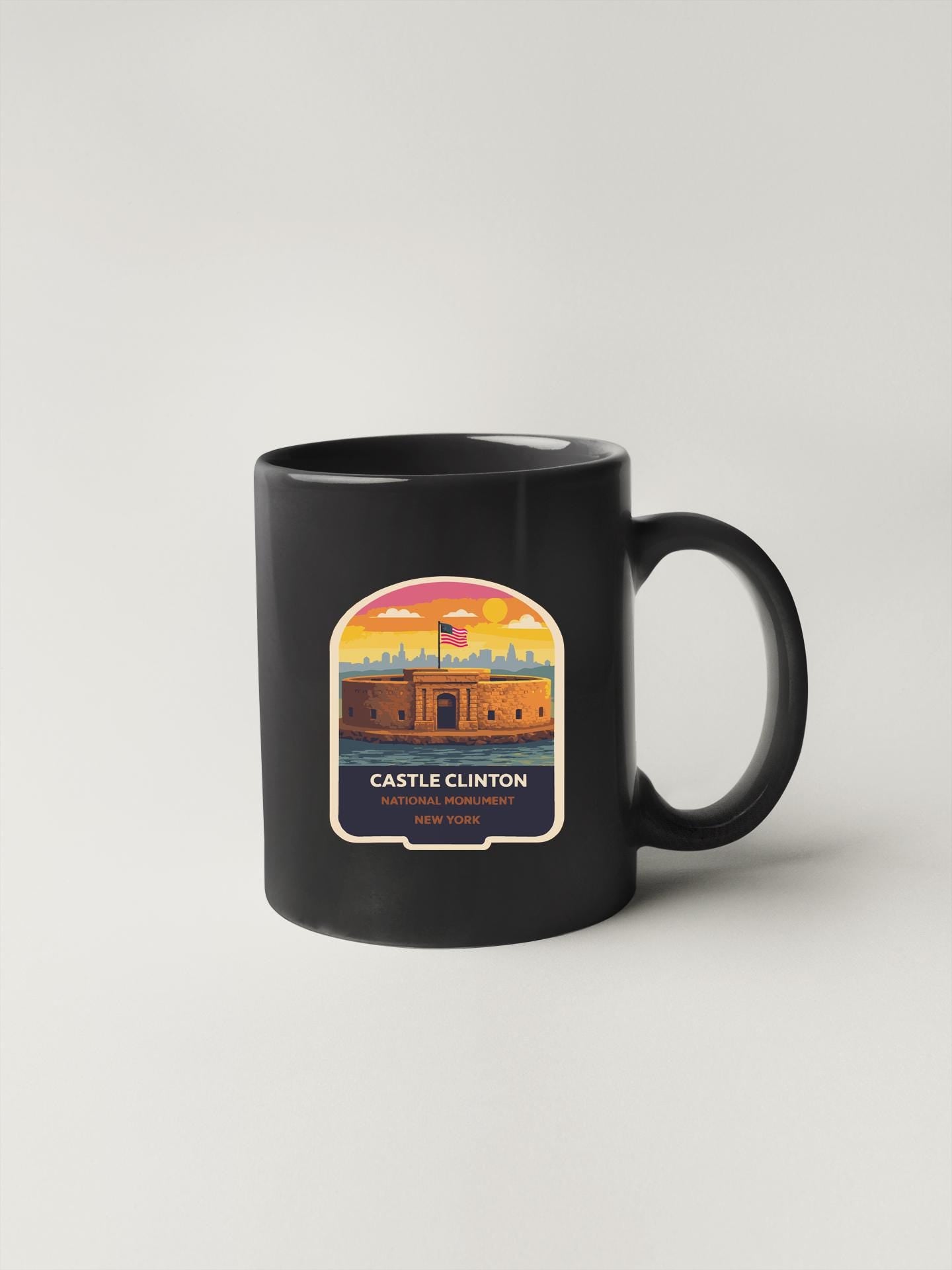 A black coffee mug with a colorful illustration of Castle Clinton, a historic fortification in New York, on it.