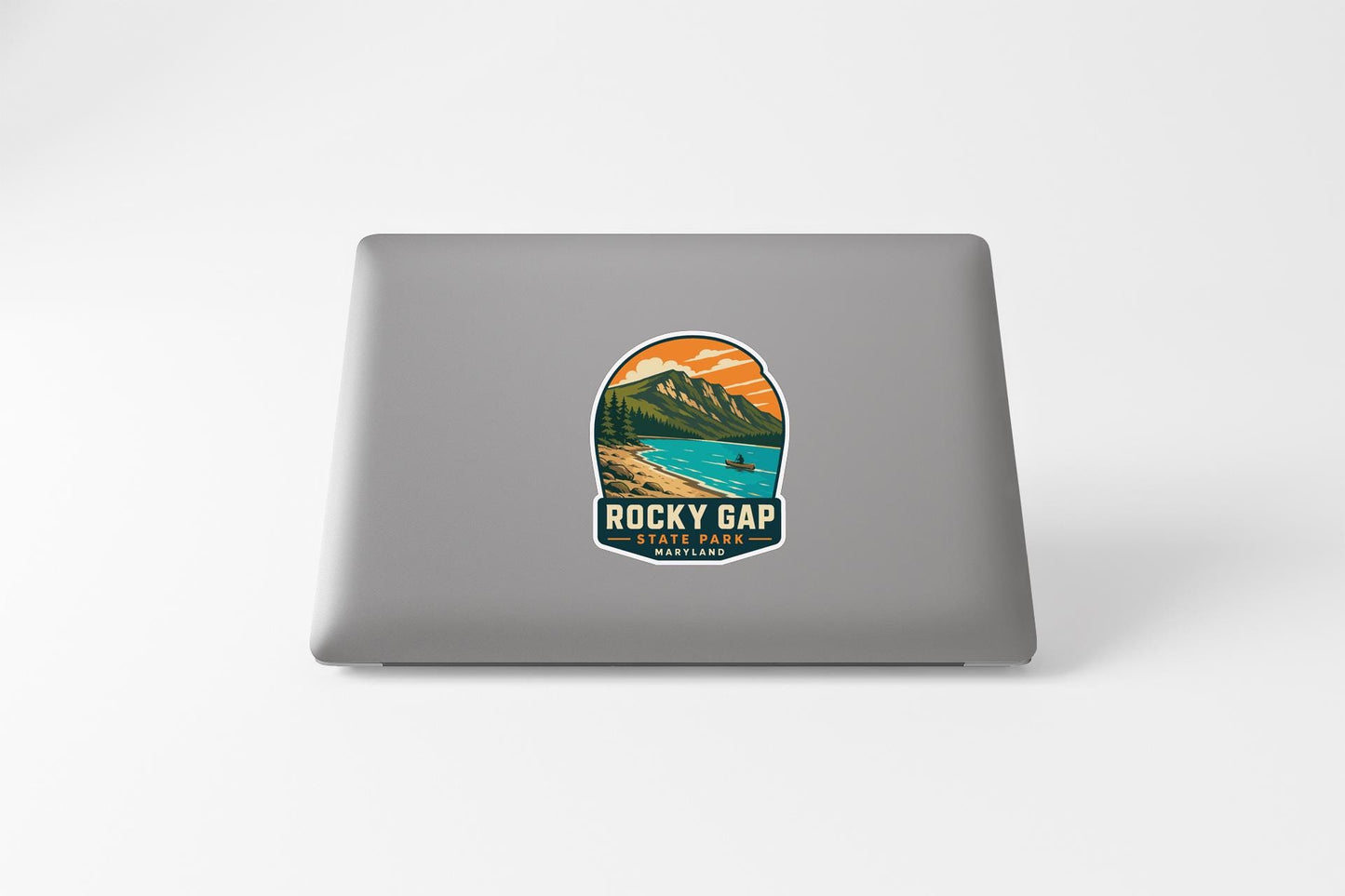 A sticker on the back of a laptop, depicting a scenic mountain landscape with a lake and a person in the distance.