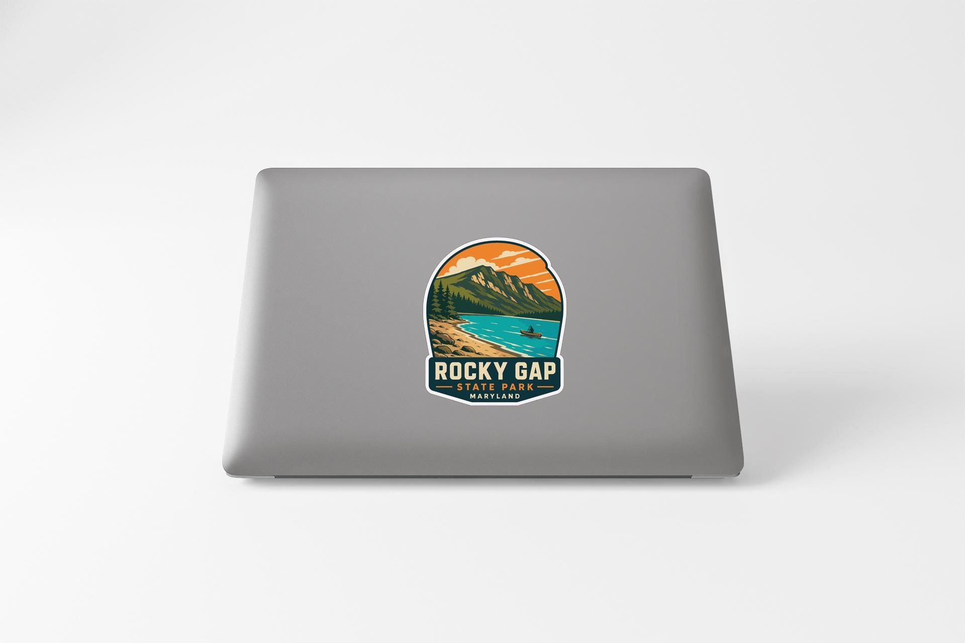 A sticker on the back of a laptop, depicting a scenic mountain landscape with a lake and a person in the distance.