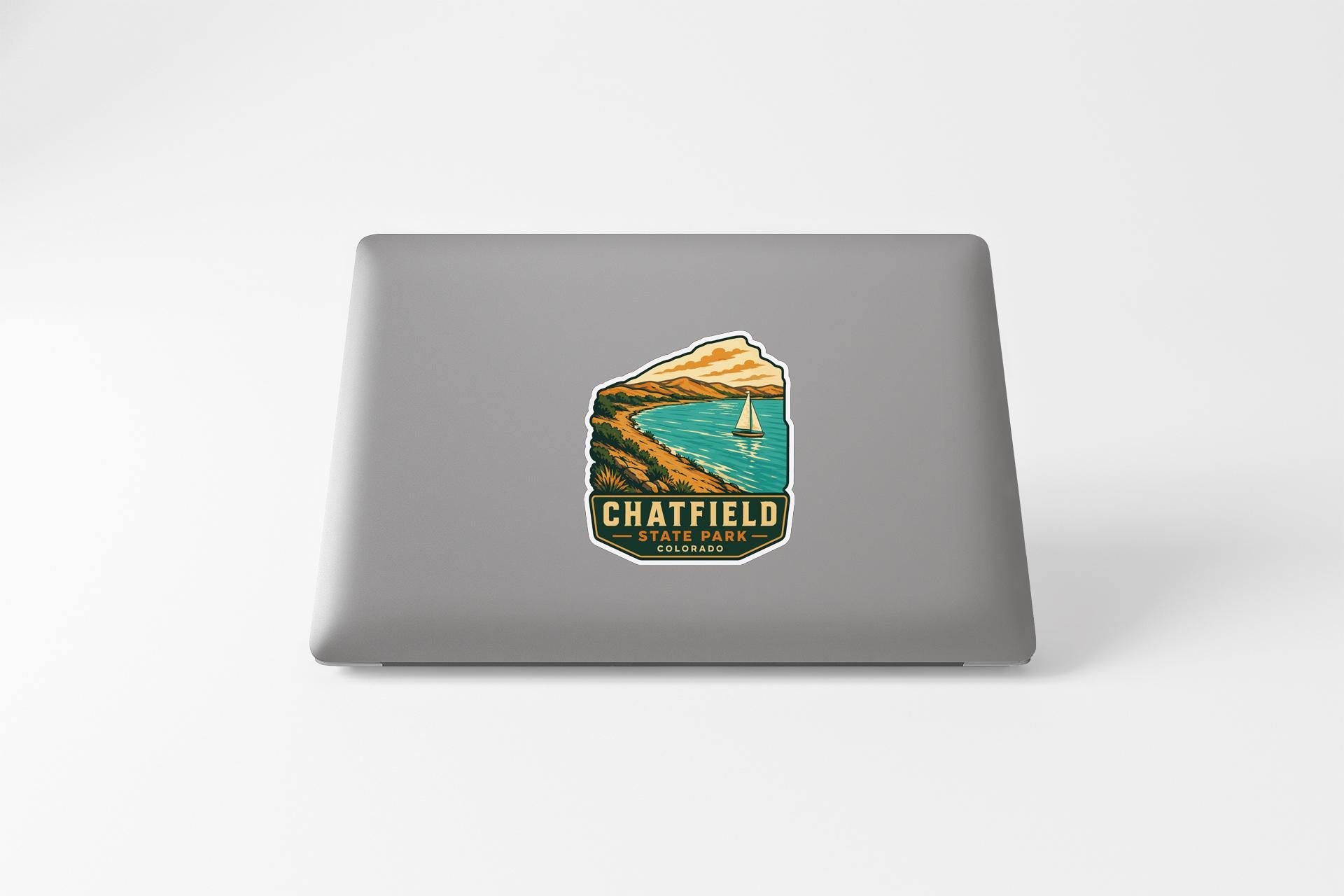 A sticker on the back of a laptop, depicting a scenic landscape with a sailboat on a lake.