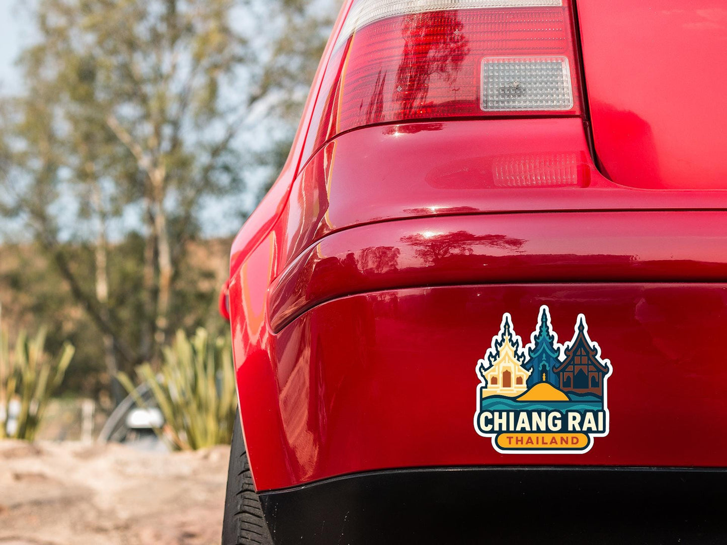 the rear end of a red car with a sticker on the trunk that says "CHIANG RAI CHIANGLAND".