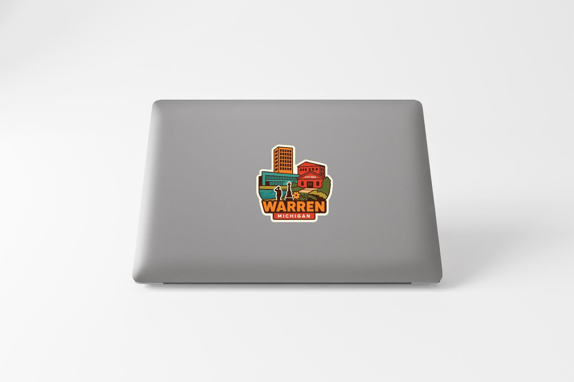 A sticker on the back of a laptop displaying an illustration of a city skyline with the text "WARREN MICHIGAN" below it.