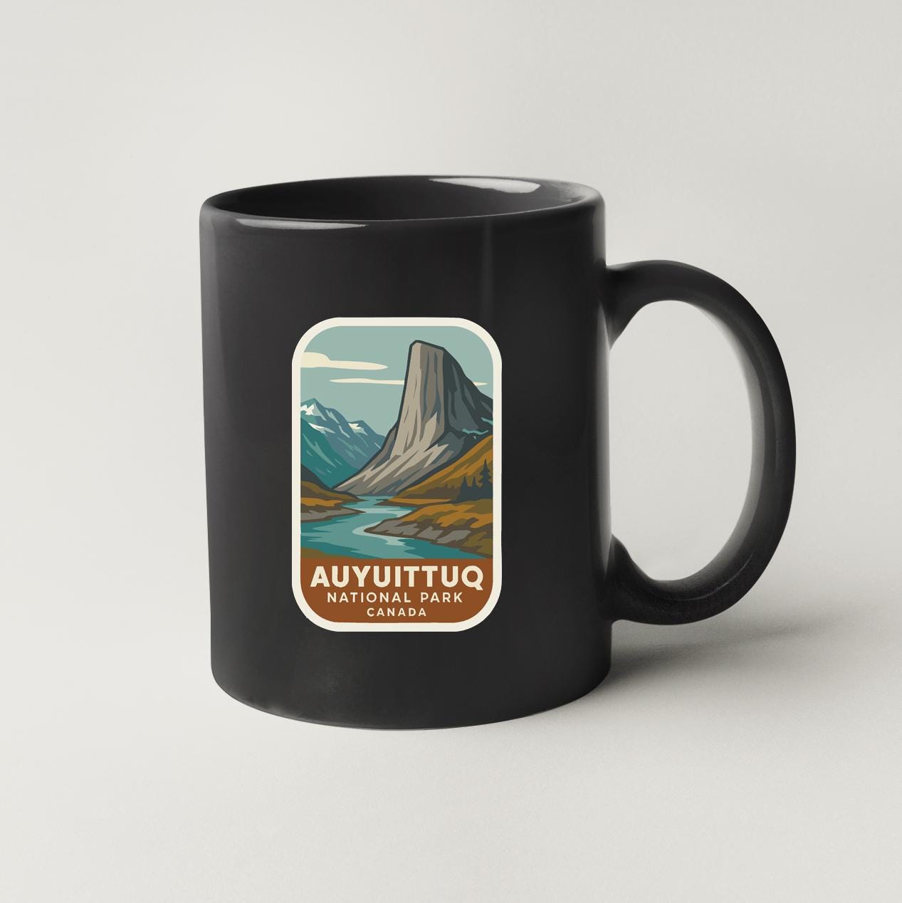 A black coffee mug with a label that says "AUYUITTUQ NATIONAL PARK CANADA".