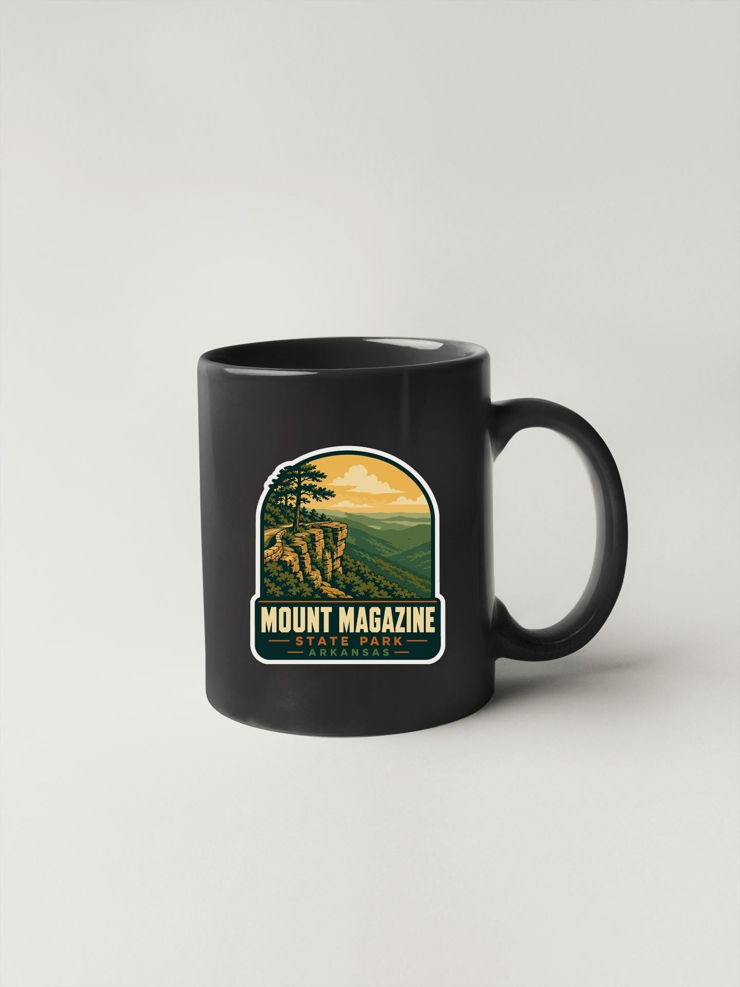 A black coffee mug with a graphic design depicting a scenic mountain landscape.