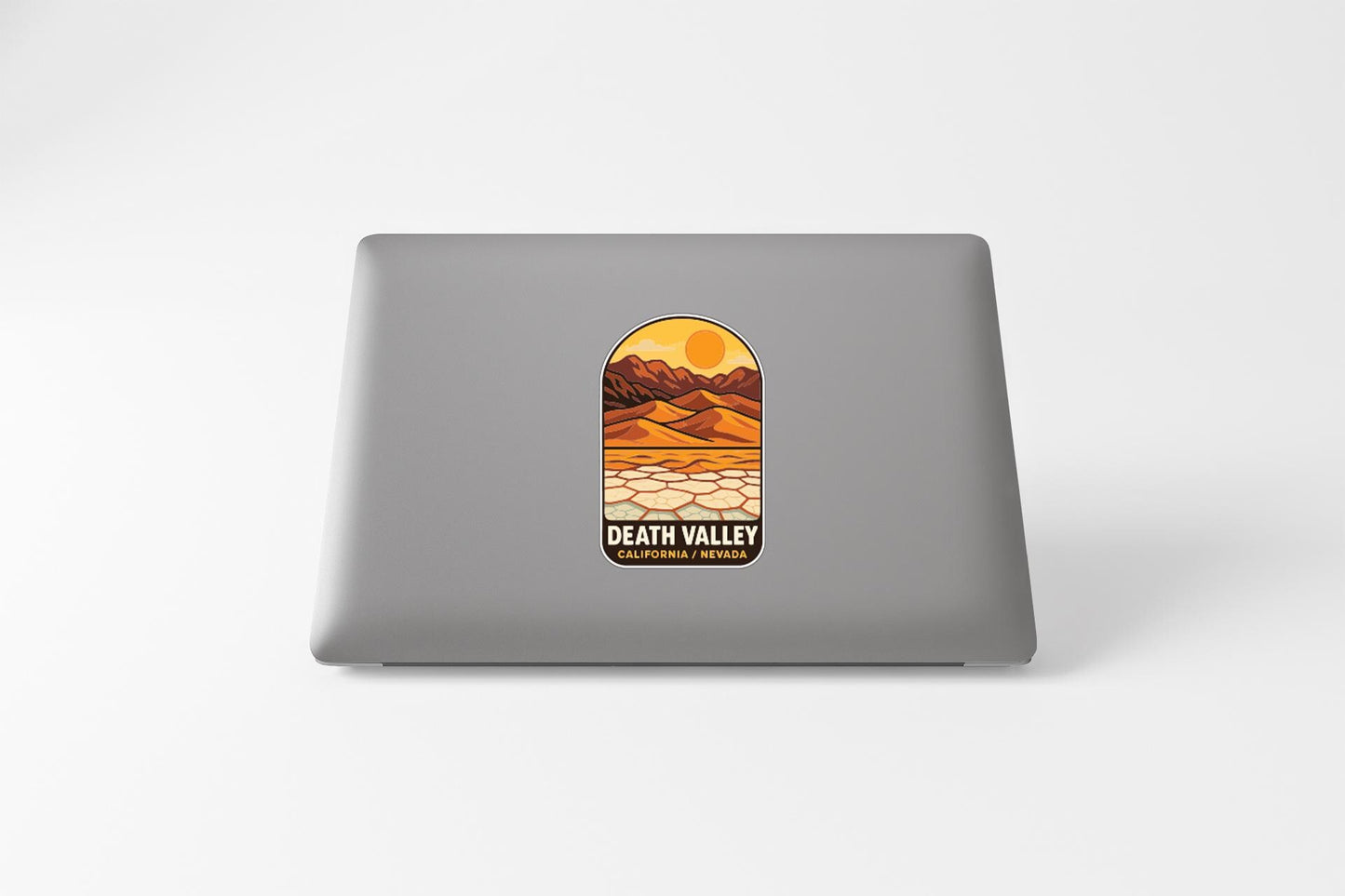a sticker on the back of a laptop that depicts a desert landscape with mountains and a sun.