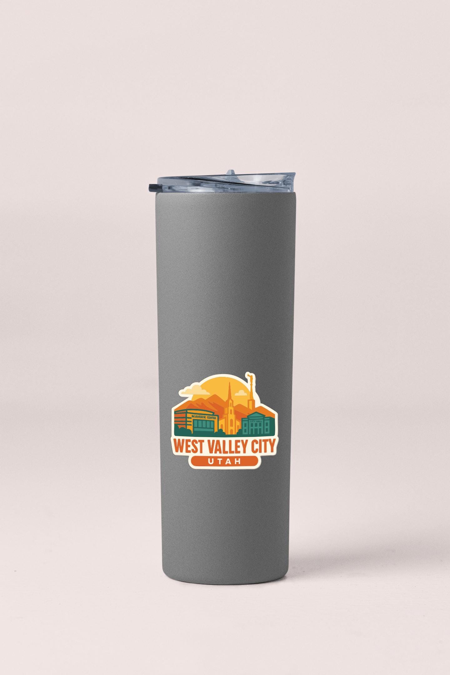 A gray insulated tumbler with a lid and a sticker featuring an illustration of West Valley City, Utah.