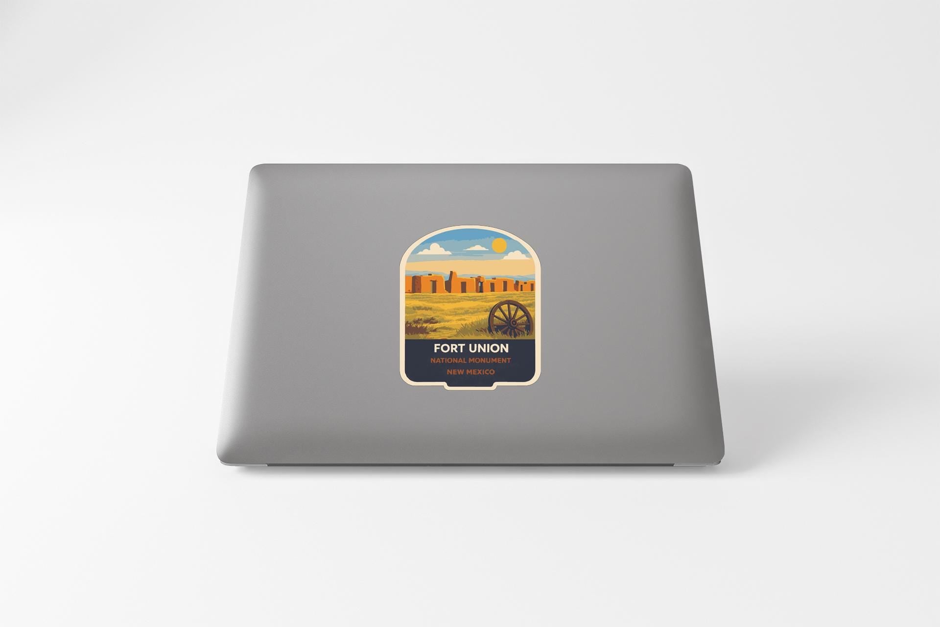 a sticker on the back of a laptop, depicting a desert landscape with a wagon wheel in the foreground.