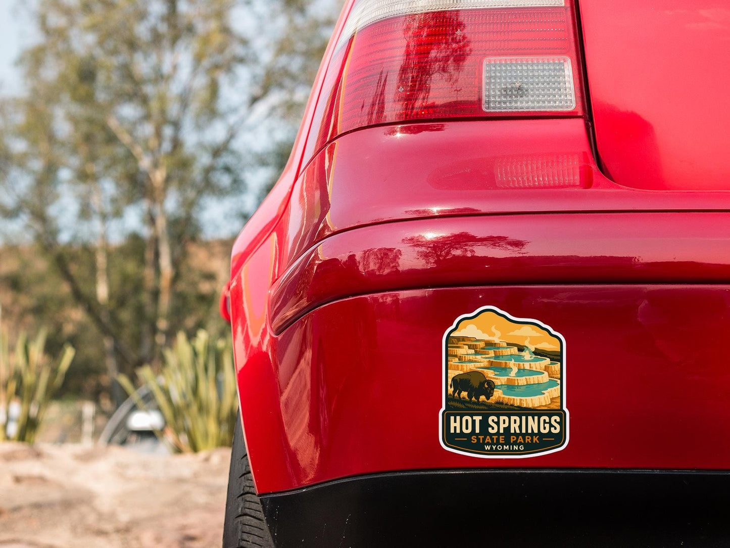 the rear end of a red car with a sticker on the back window that says "Hot Springs State Park, Wyoming".