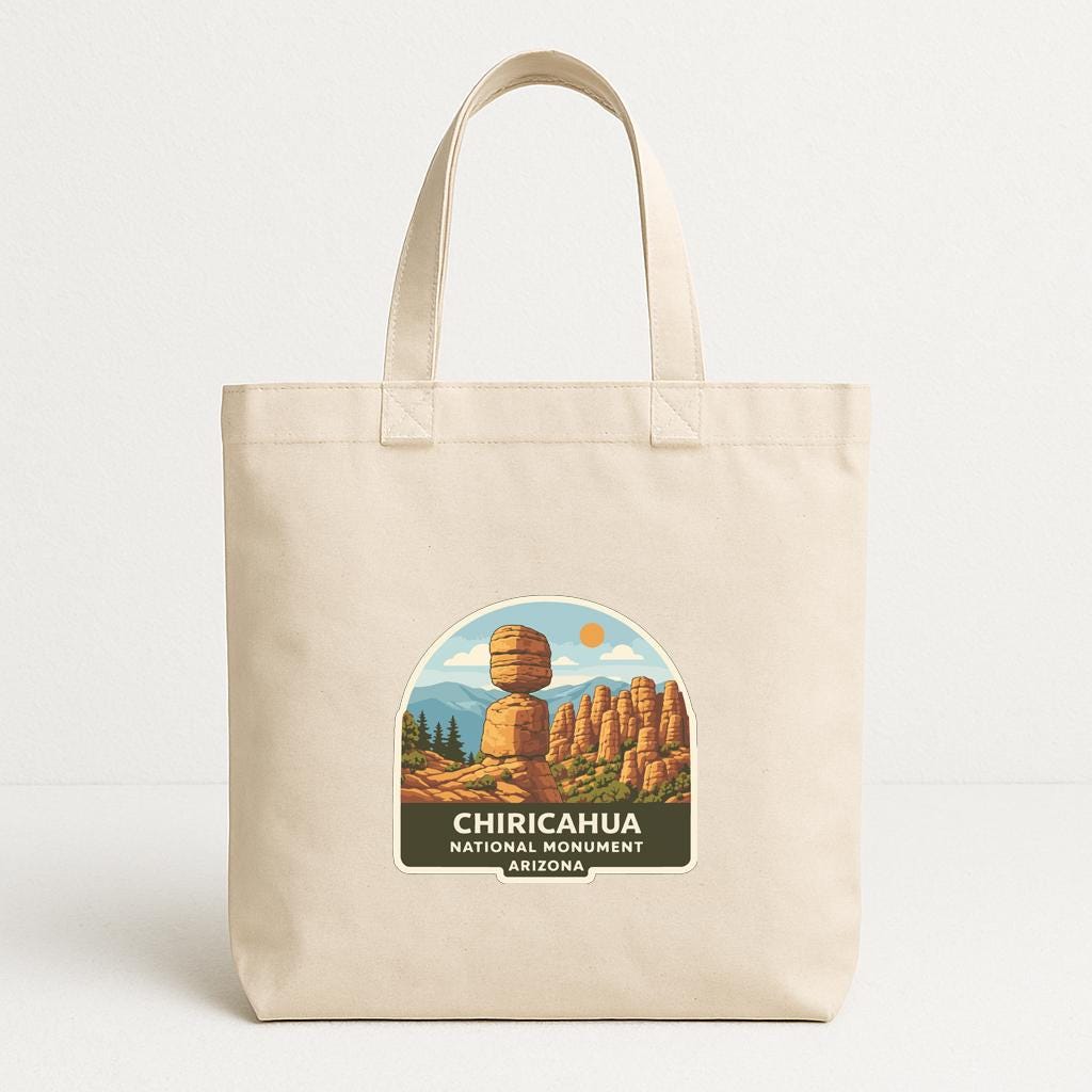 A beige tote bag with a printed label that says "CHICAHUA NATIONAL MONUMENT ARIZONA" depicting a scenic landscape with rock formations and a sun.