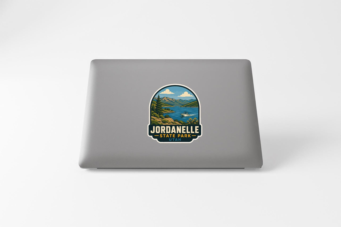 A sticker on the back of a laptop that features a scenic landscape with mountains, a lake, and a forest.