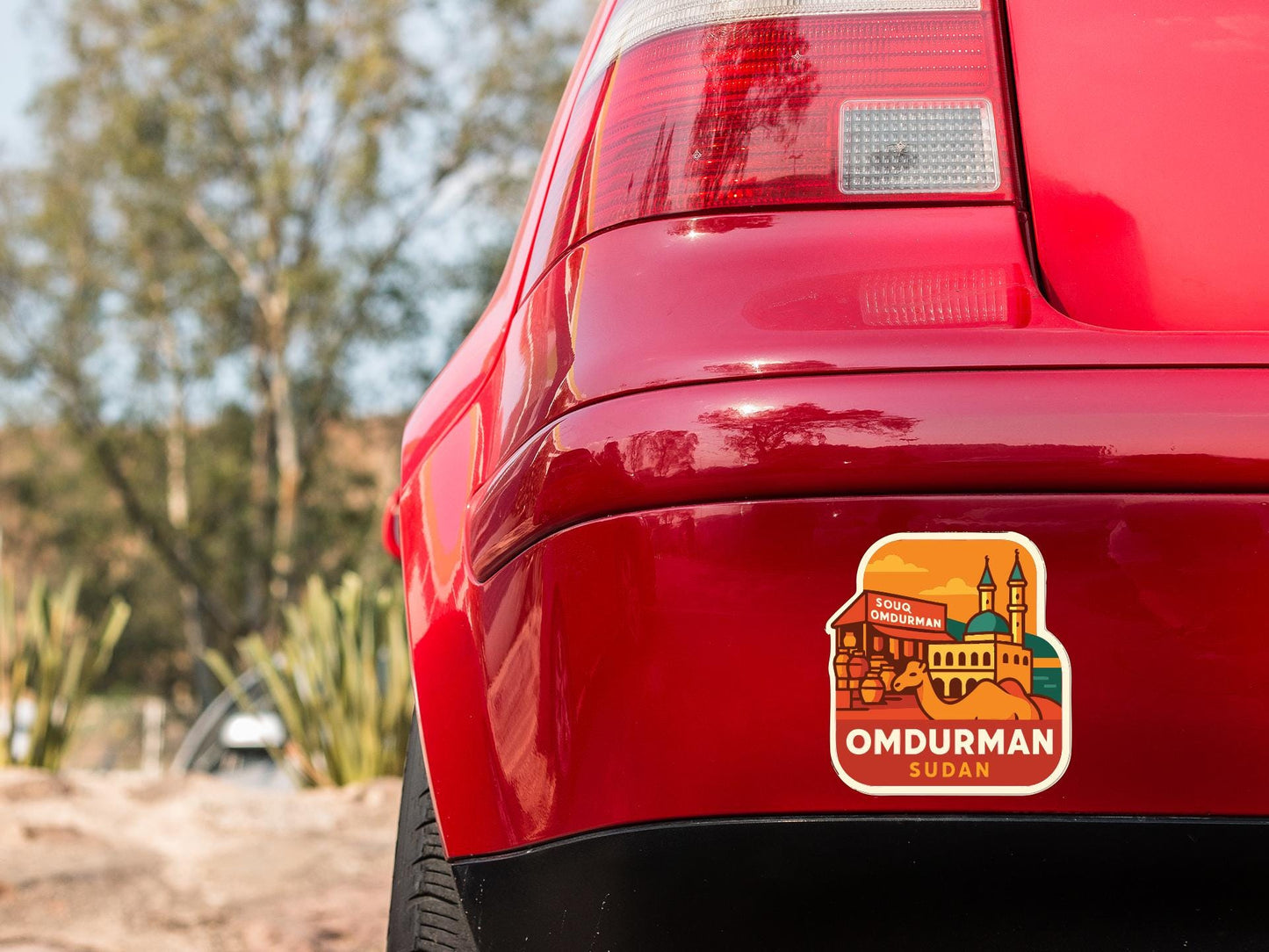 the rear end of a red car with a sticker on the trunk that says "OMDURMAN SUZAN".