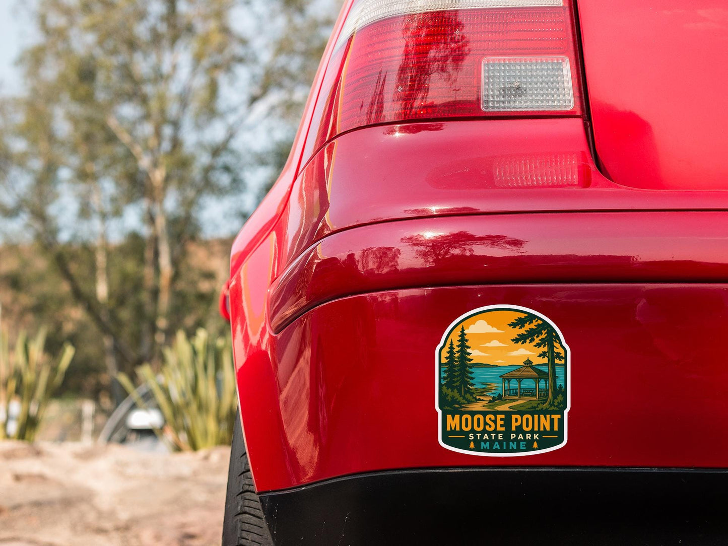 the rear end of a red car with a sticker on the back window that says " Moose Point State Park Maine".