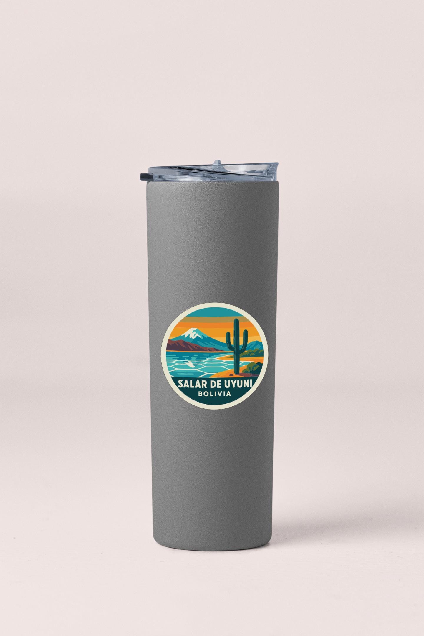 A gray insulated tumbler with a sticker on it, featuring a desert landscape with a mountain and a cactus.