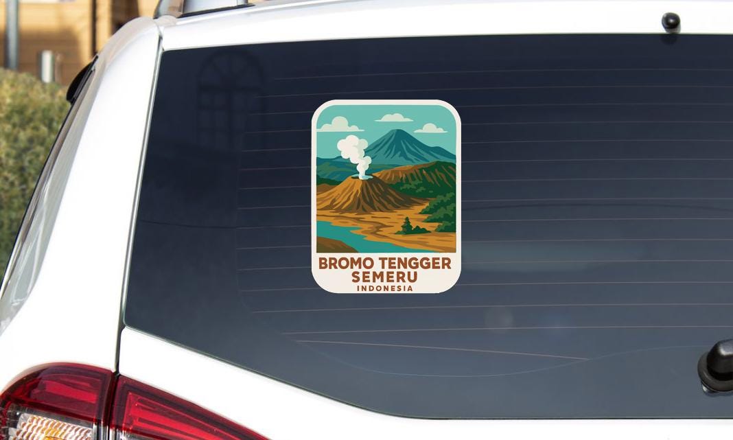 A sticker on the rear window of a car, depicting a scenic landscape with mountains, a river, and a volcano.