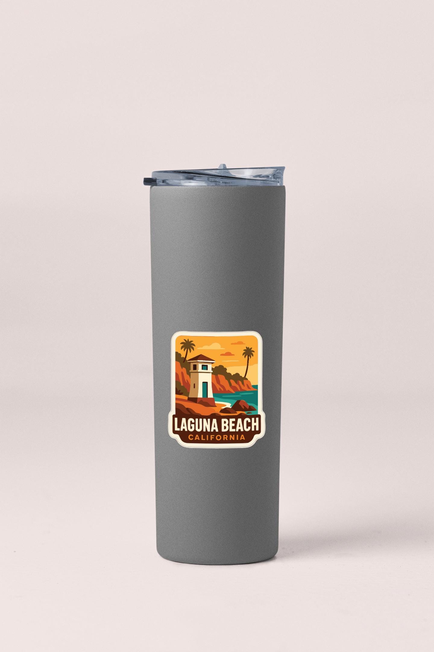 A gray insulated tumbler with a sticker depicting a beach scene and the text "LAGUNA BEACH, CALIFORNIA".