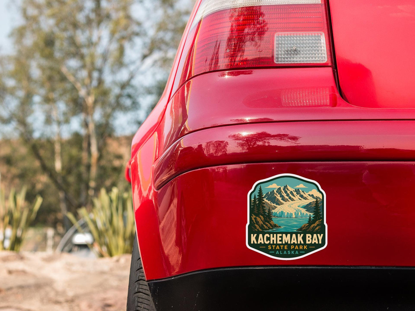 the rear end of a red car with a sticker on the trunk that says "Kachemak Bay State Park Alaska".