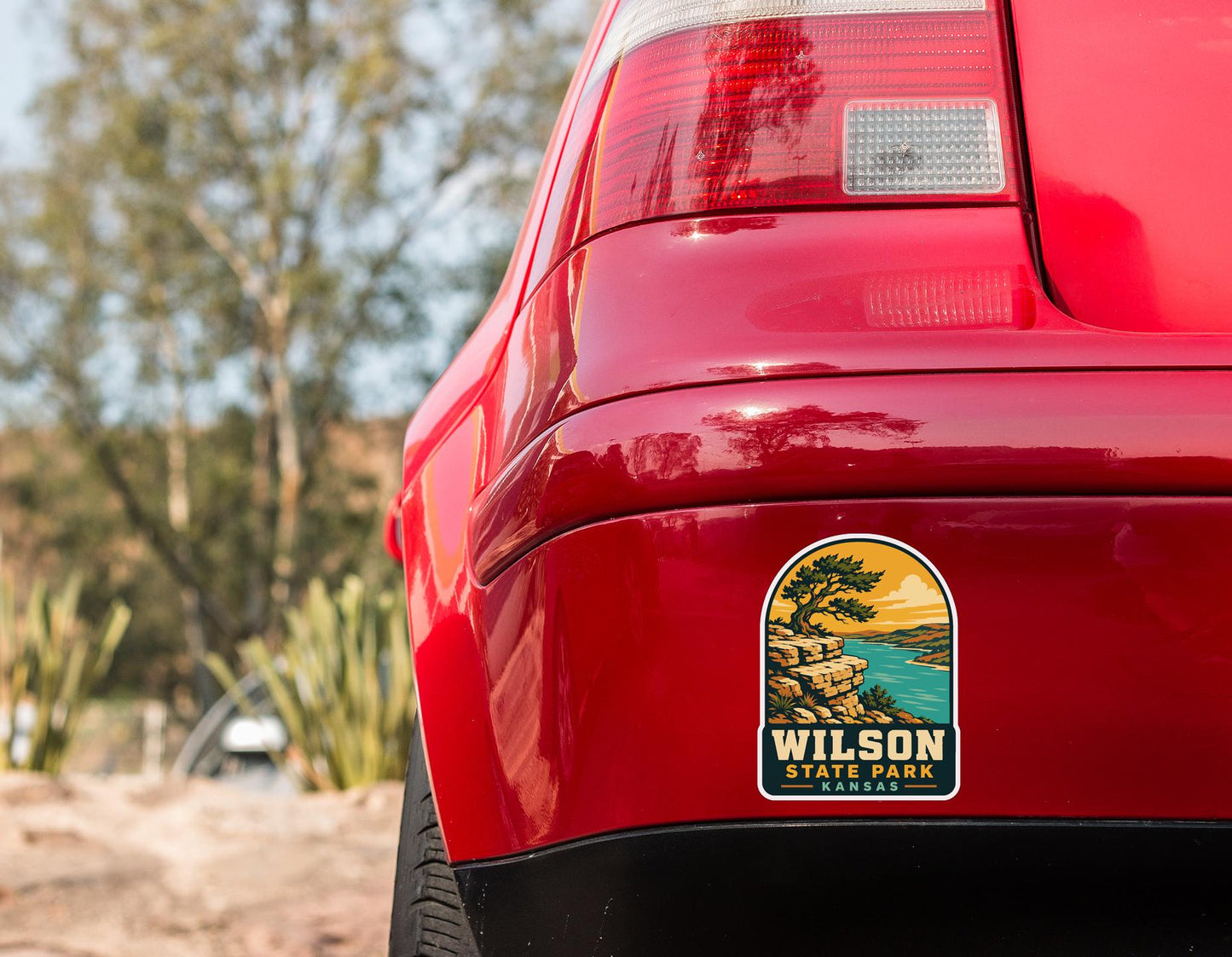 the rear end of a red car with a sticker on the trunk that says "Wilson State Park Kansas".