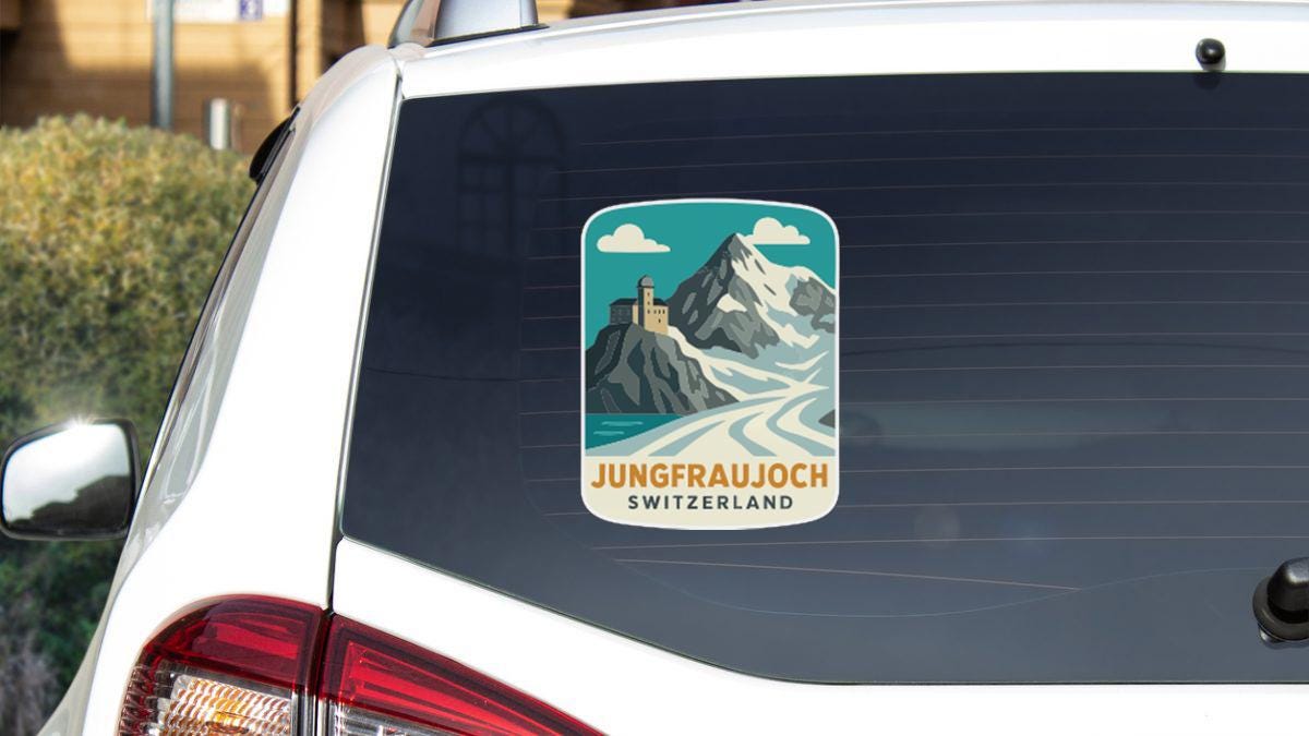 A sticker on the rear window of a car, depicting a mountain landscape with a castle or tower in the background.