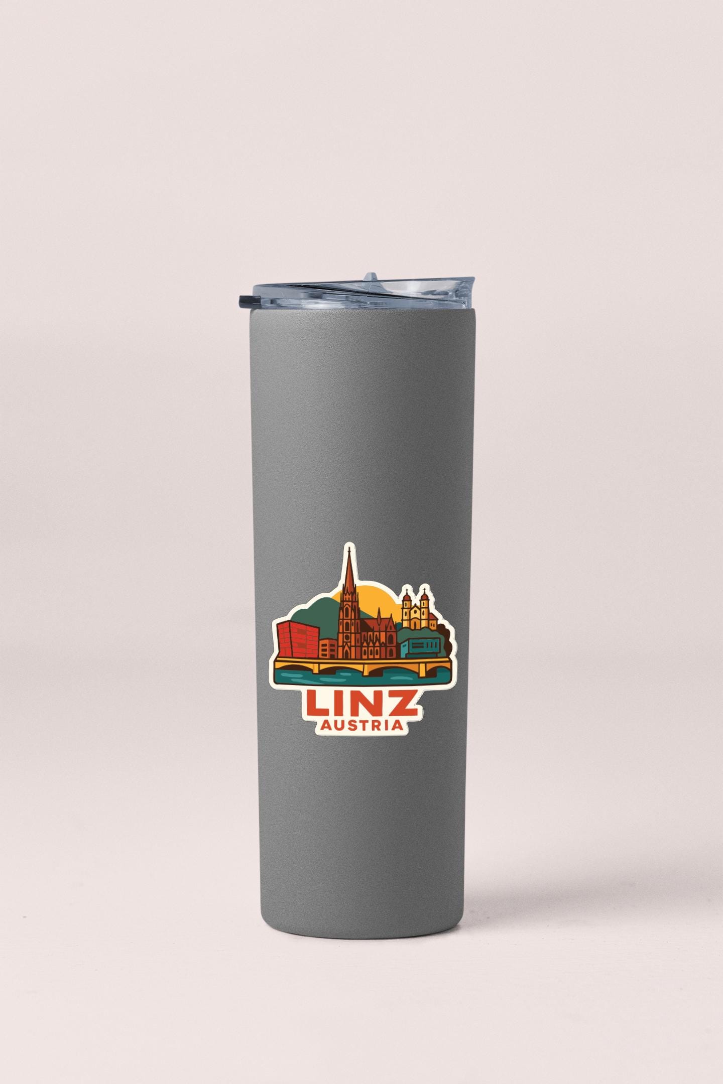 A gray insulated tumbler with a sticker depicting the city of Linz, Austria.