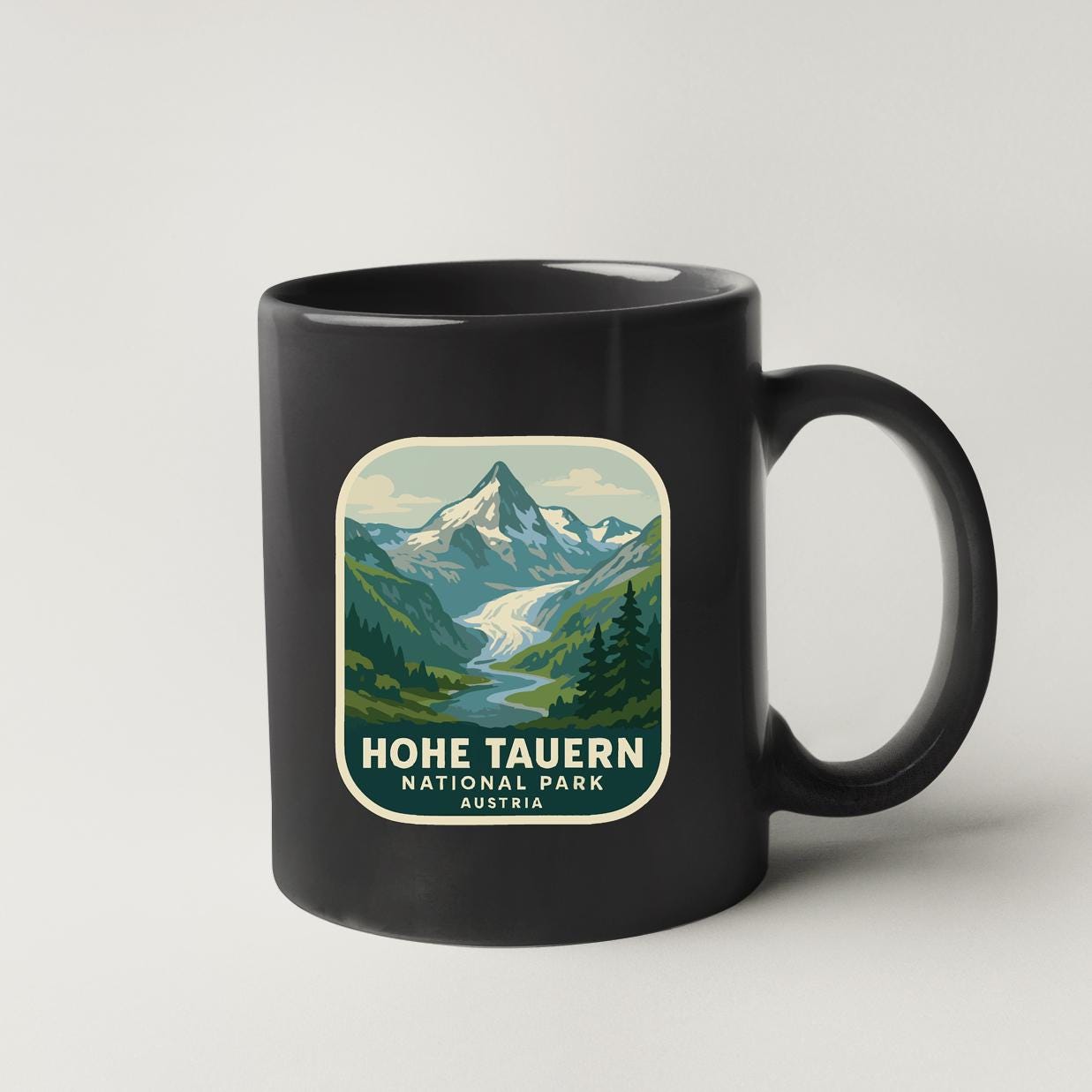 A black coffee mug with a graphic design depicting a mountain landscape and a river.