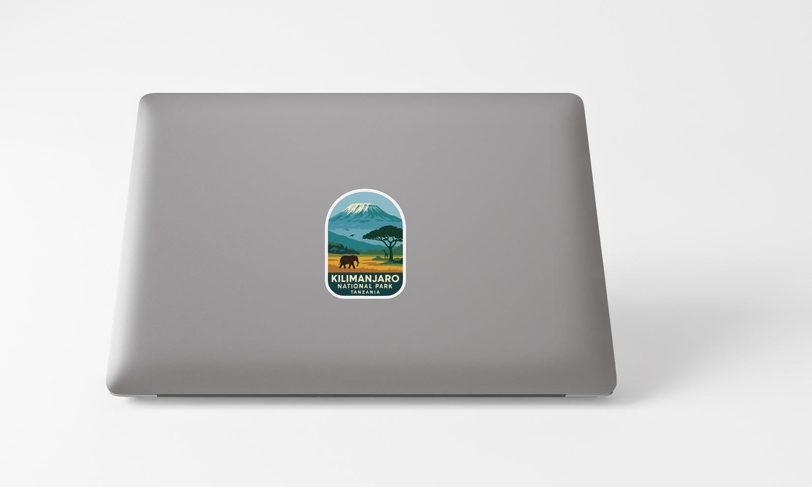 A sticker with a mountain landscape and a small animal, likely a bear, is placed on the back of a laptop computer.