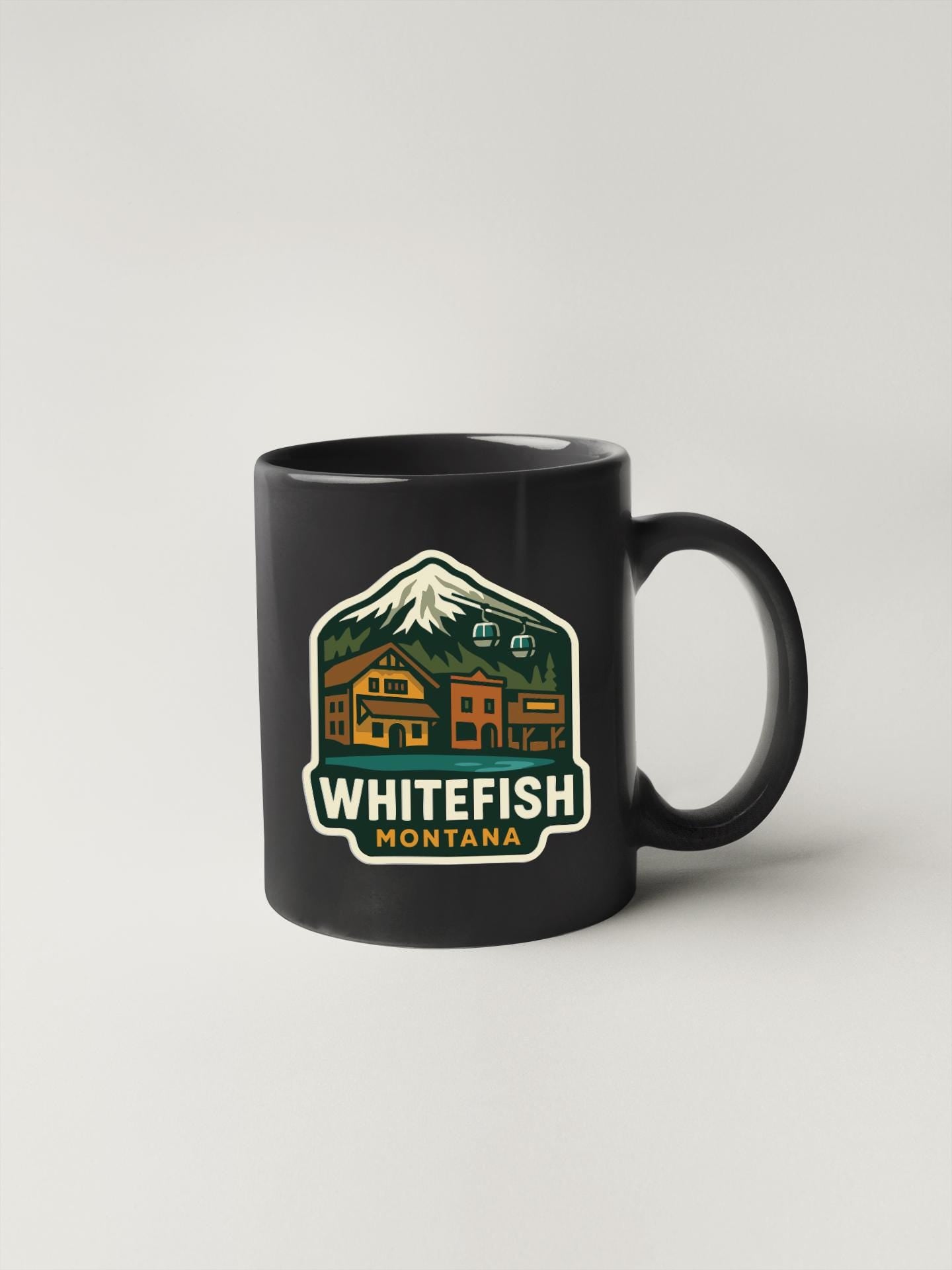 A black coffee mug with a graphic design depicting a mountain landscape and a lodge, along with the text "WHITEFISH MONTANA".