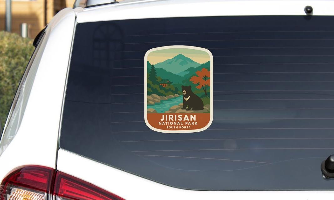 A sticker on the rear window of a car, depicting a scenic landscape with mountains, trees, and a bear.