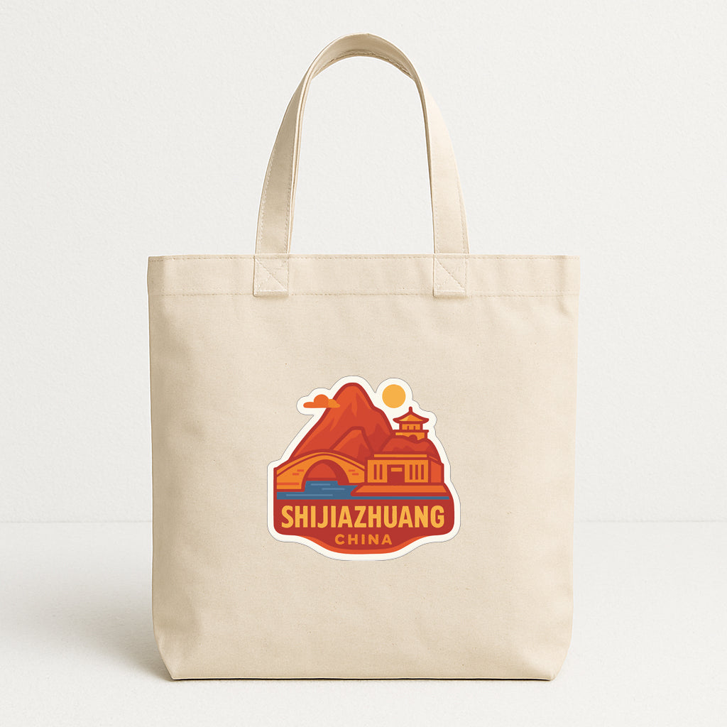 A beige tote bag with a colorful graphic design depicting a mountain and a building, along with the text "SHIJIZHUANG CHINA".