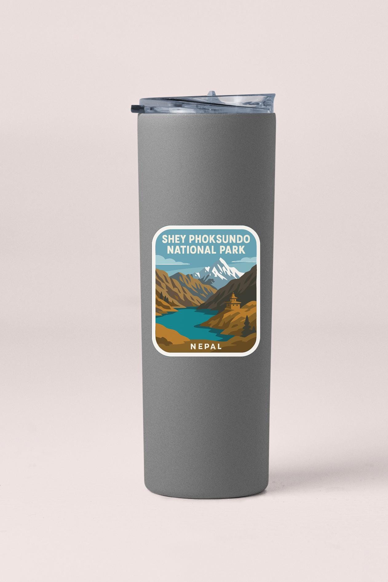 A gray insulated tumbler with a sticker depicting the Shey Phoksuundo National Park in Nepal.