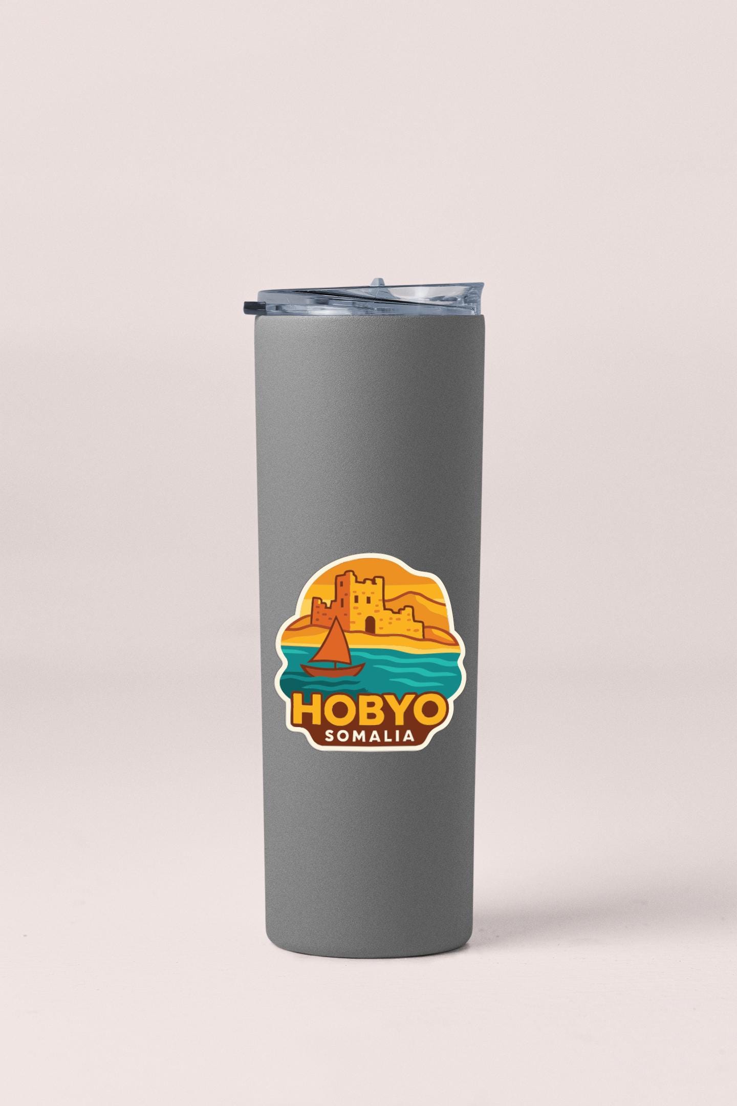 A gray insulated tumbler with a sticker depicting a castle and a sailboat, along with the text "HOBBYO SOMALIA".