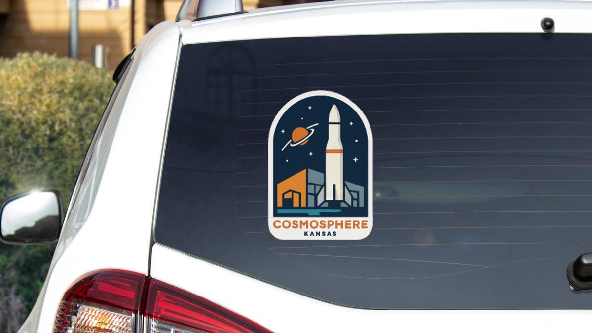 a sticker on the rear window of a vehicle, depicting a rocket ship and a city skyline.