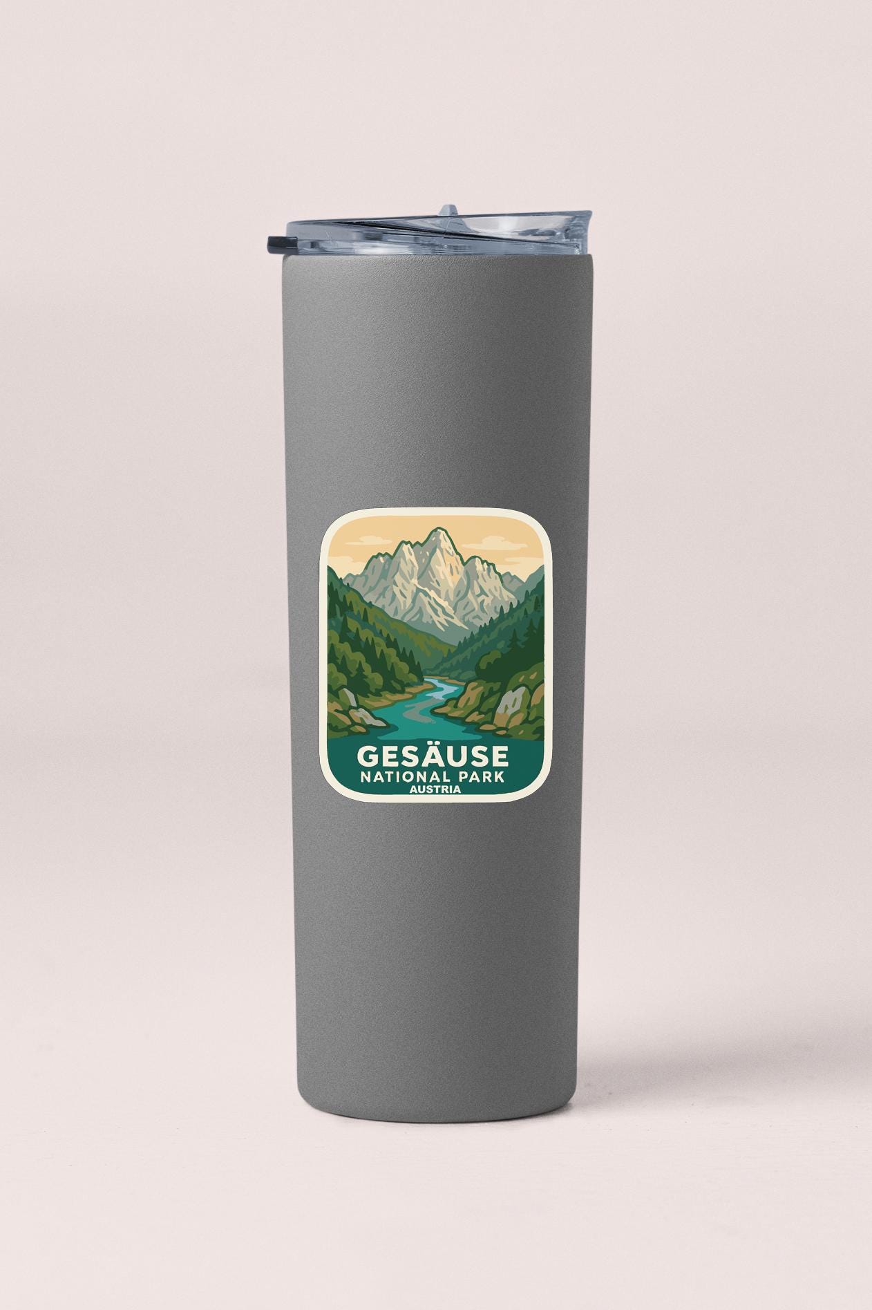 A gray insulated tumbler with a sticker depicting a mountain landscape and a river.