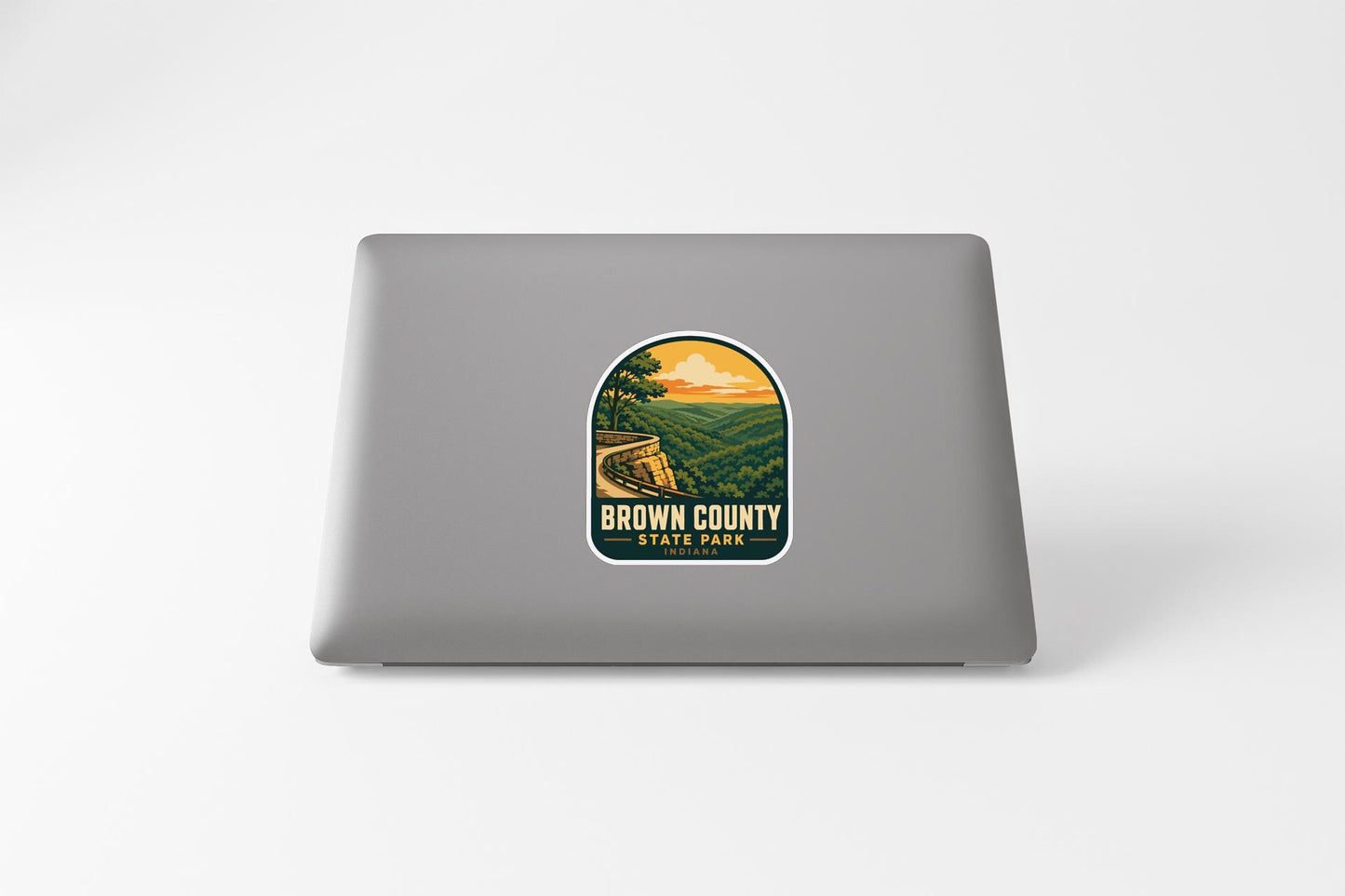 A sticker on the back of a laptop, depicting a scenic landscape with a train track and a sunset in the background.
