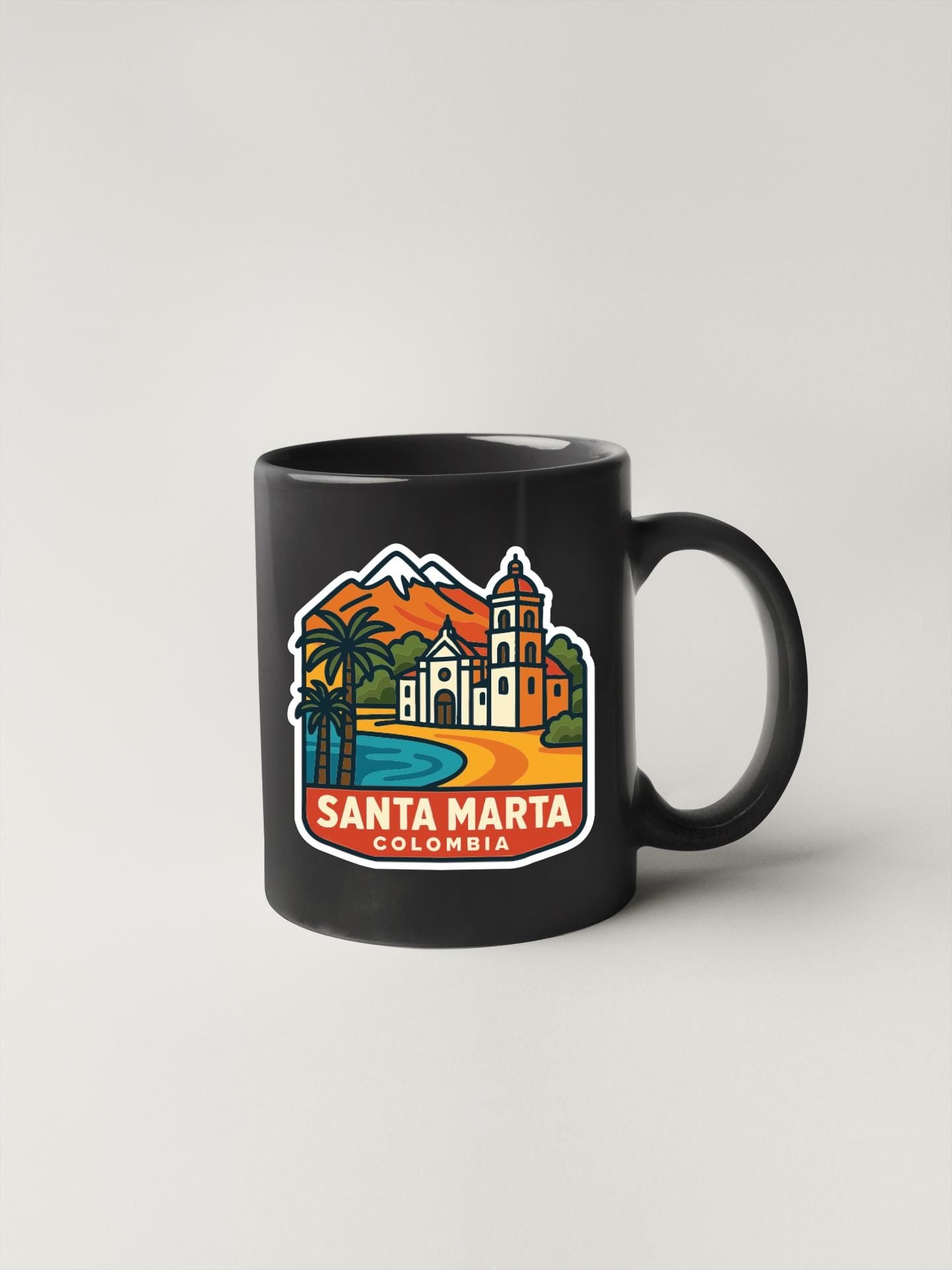A black coffee mug with a colorful illustration of Santa Marta, Colombia, featuring a church, palm trees, and mountains.