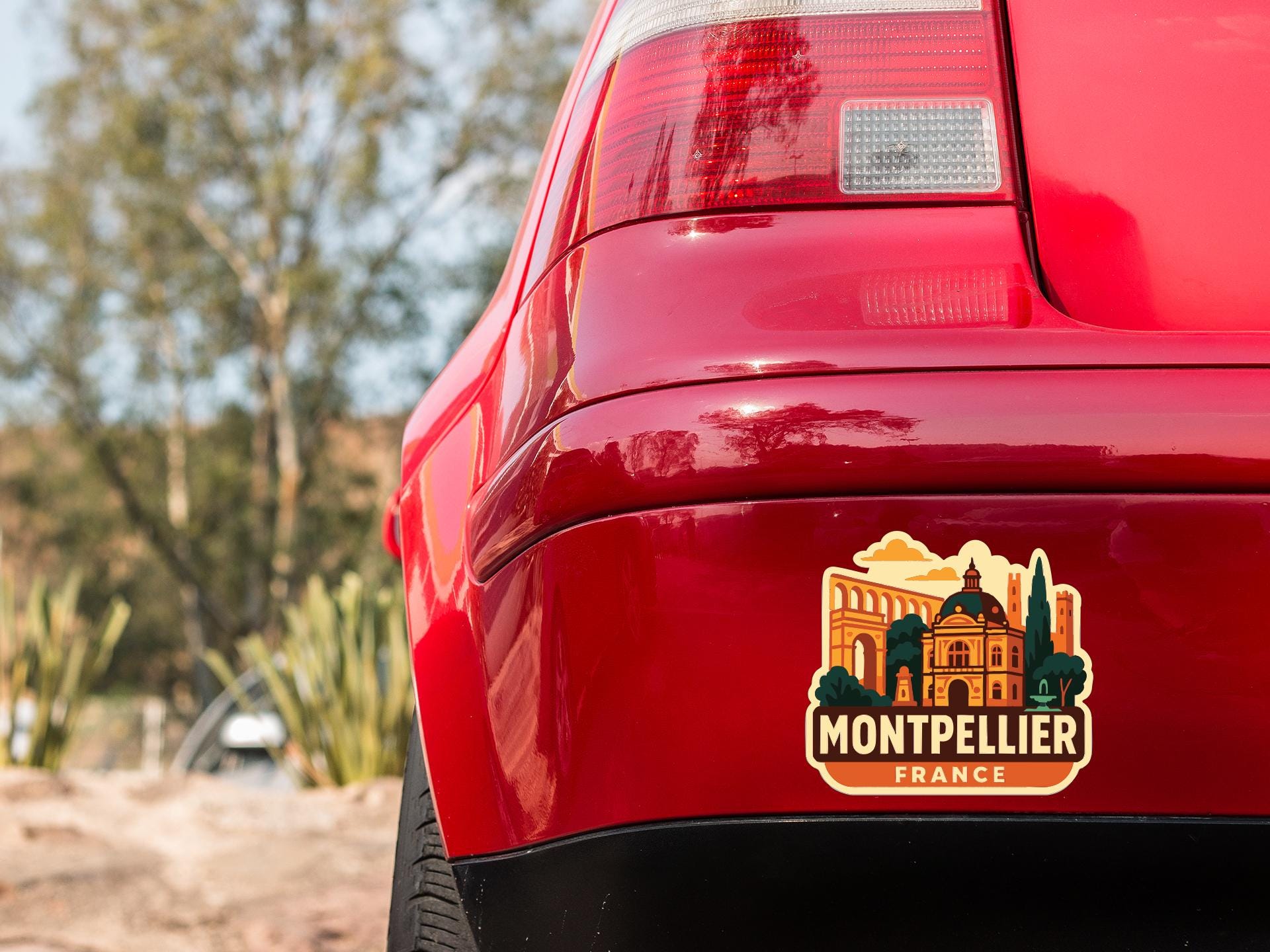 the rear end of a red car with a sticker on the trunk that features a scenic image of a building and landscape.