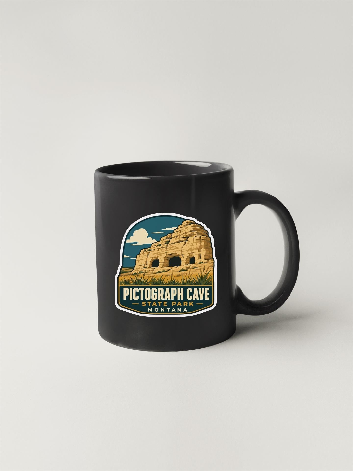 A black coffee mug with a graphic design depicting the Pictograph Cave in Montana.